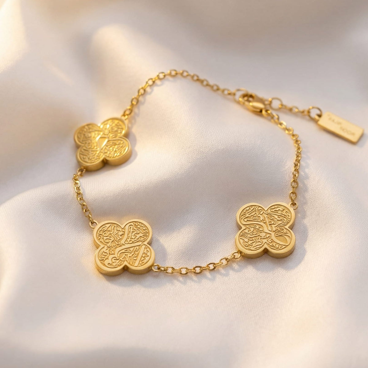 Gold bracelet with clover-shaped charms on a soft white fabric background
