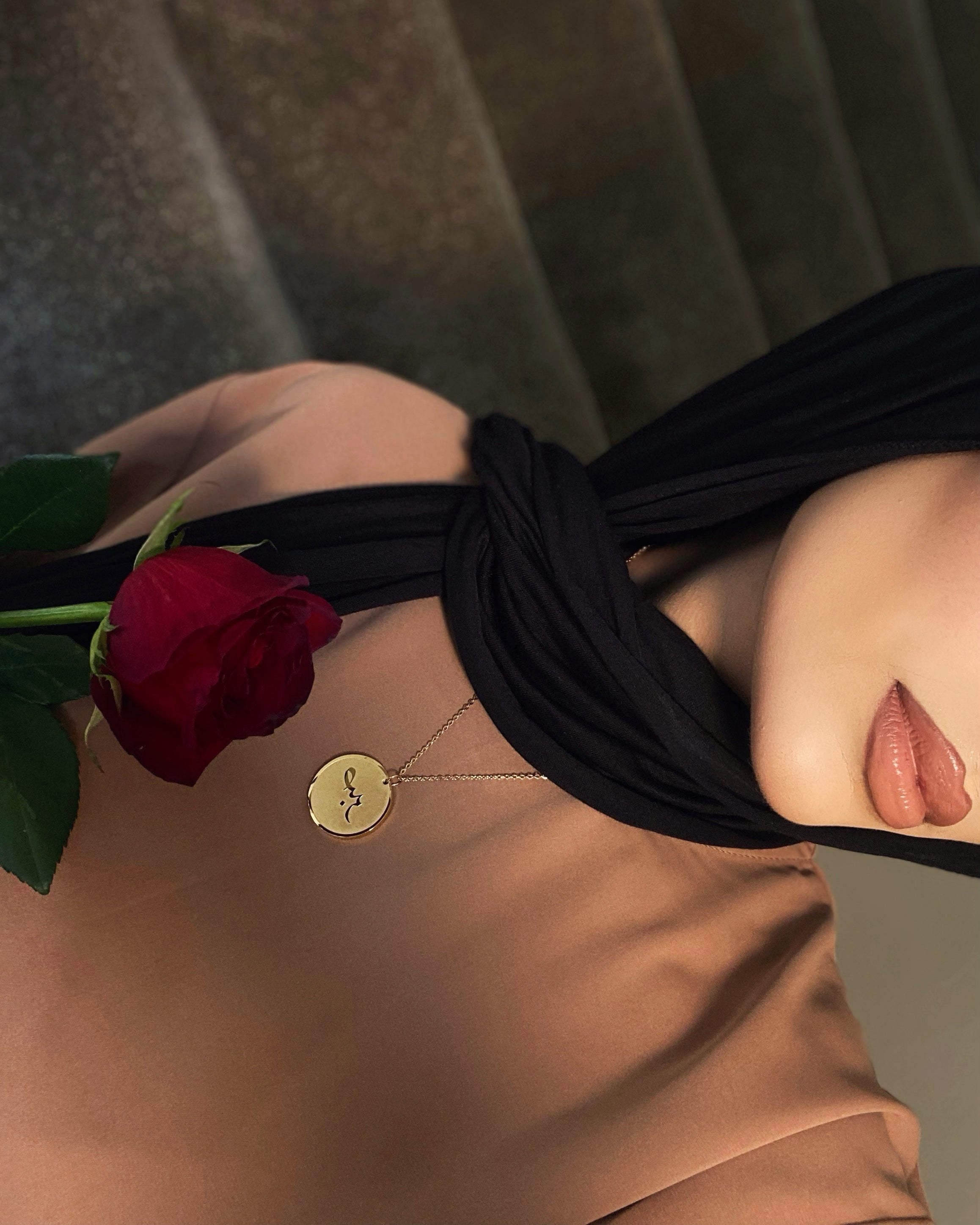 Person wearing a black headband with a red rose, sitting on a textured surface.