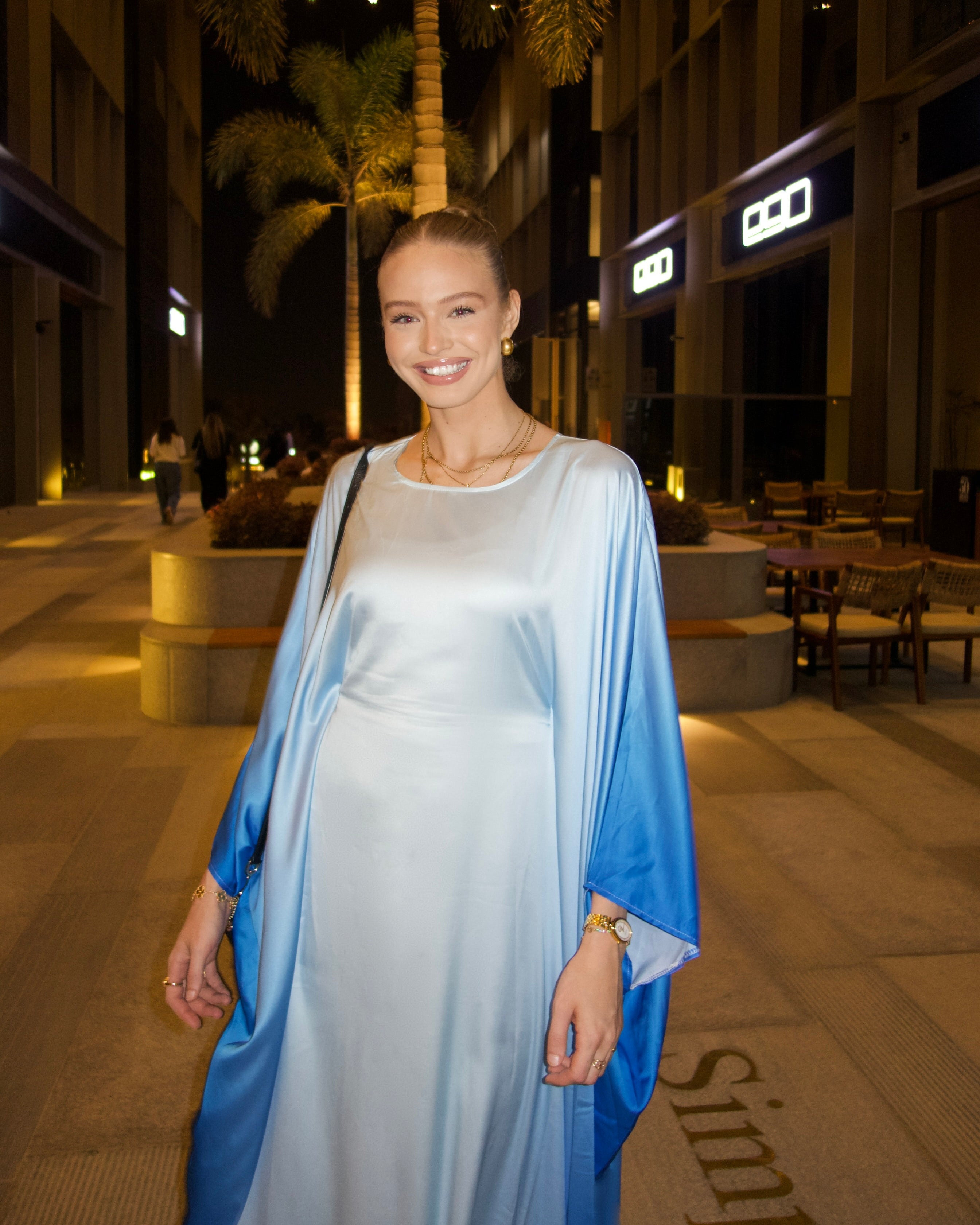 Woman in a light blue and white dress standing on a city street at night.