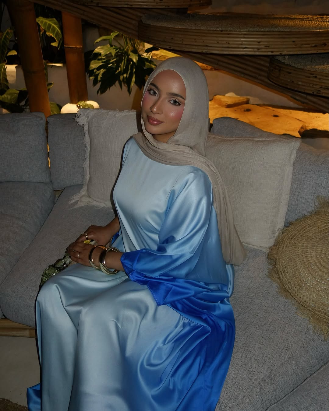 Woman in a blue dress sitting on a couch with a neutral background