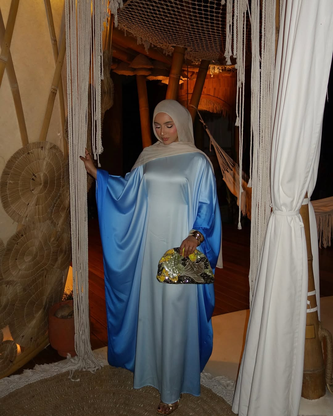 Woman in a blue dress and headscarf standing in a decorated indoor setting.