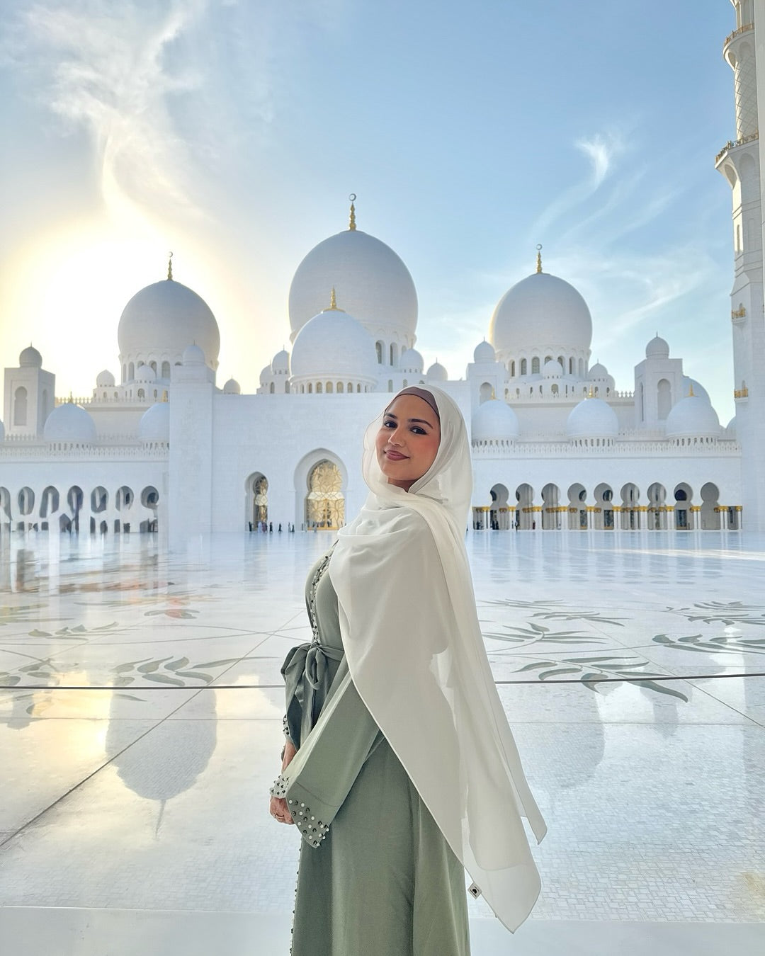 Woman in a hijab standing in front of a large white mosque with multiple domes.