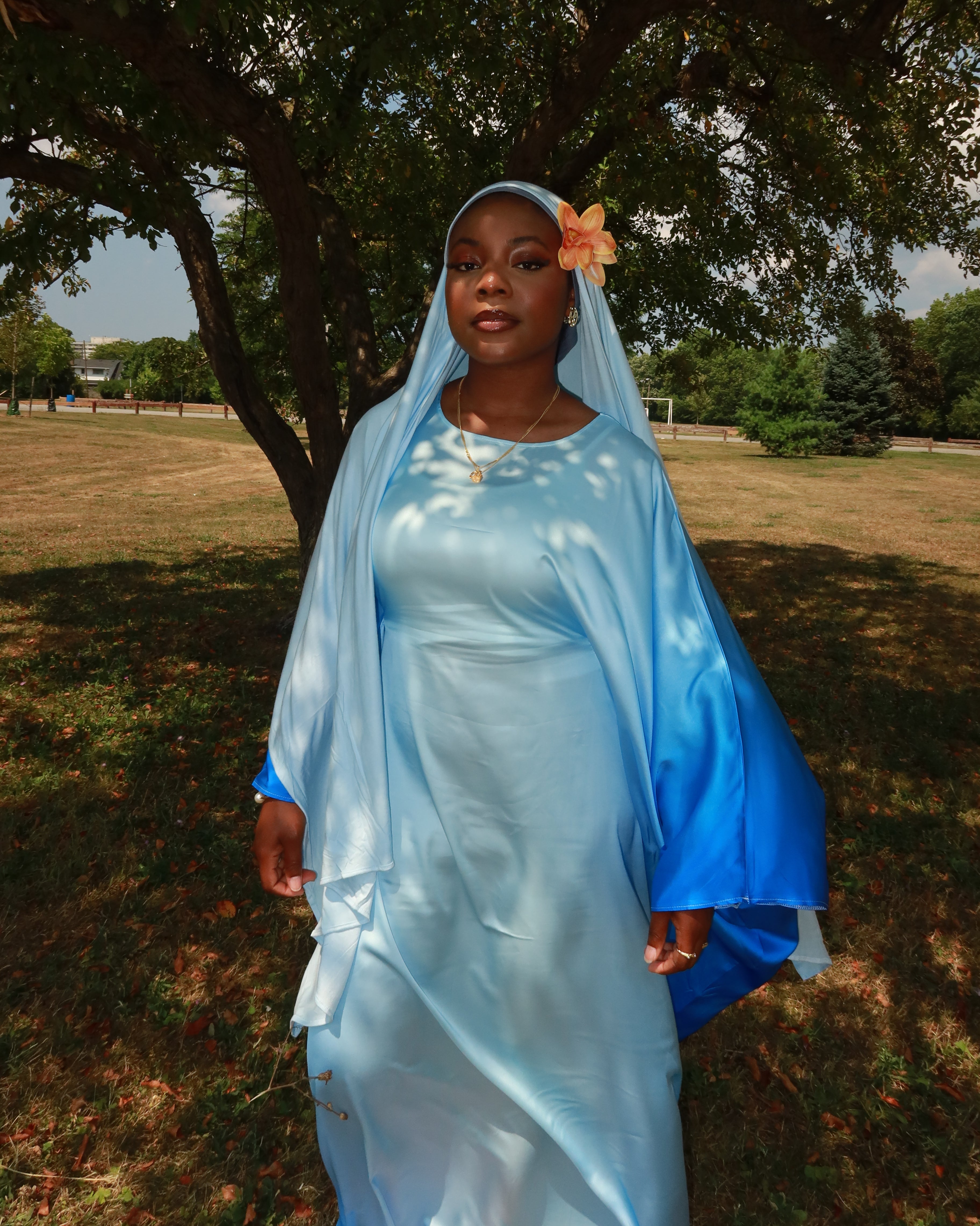 Person in a blue dress standing outdoors with trees and grass in the background