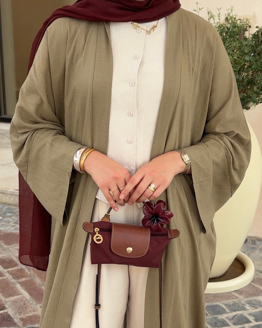 Woman wearing a long olive green cardigan over a white outfit, holding a small brown handbag.
