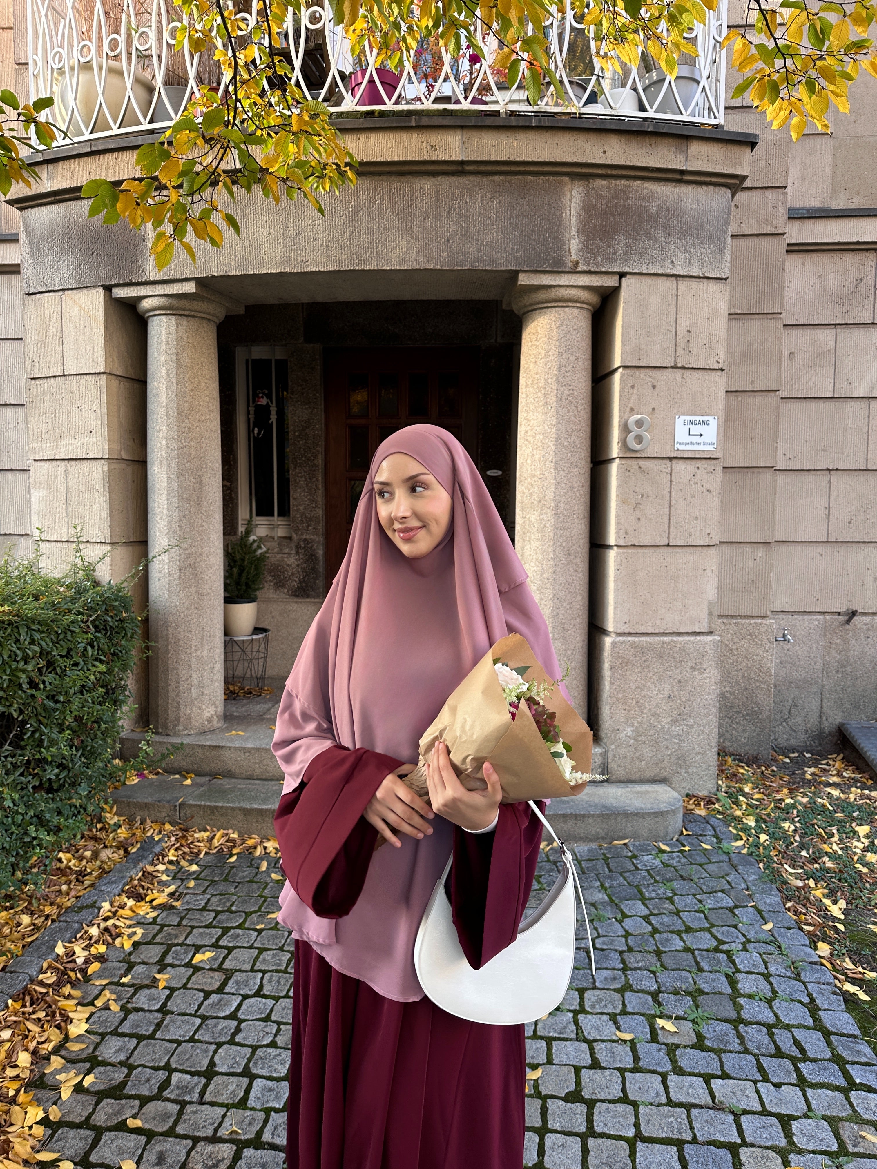 Woman in a pink hijab holding flowers in front of a building entrance