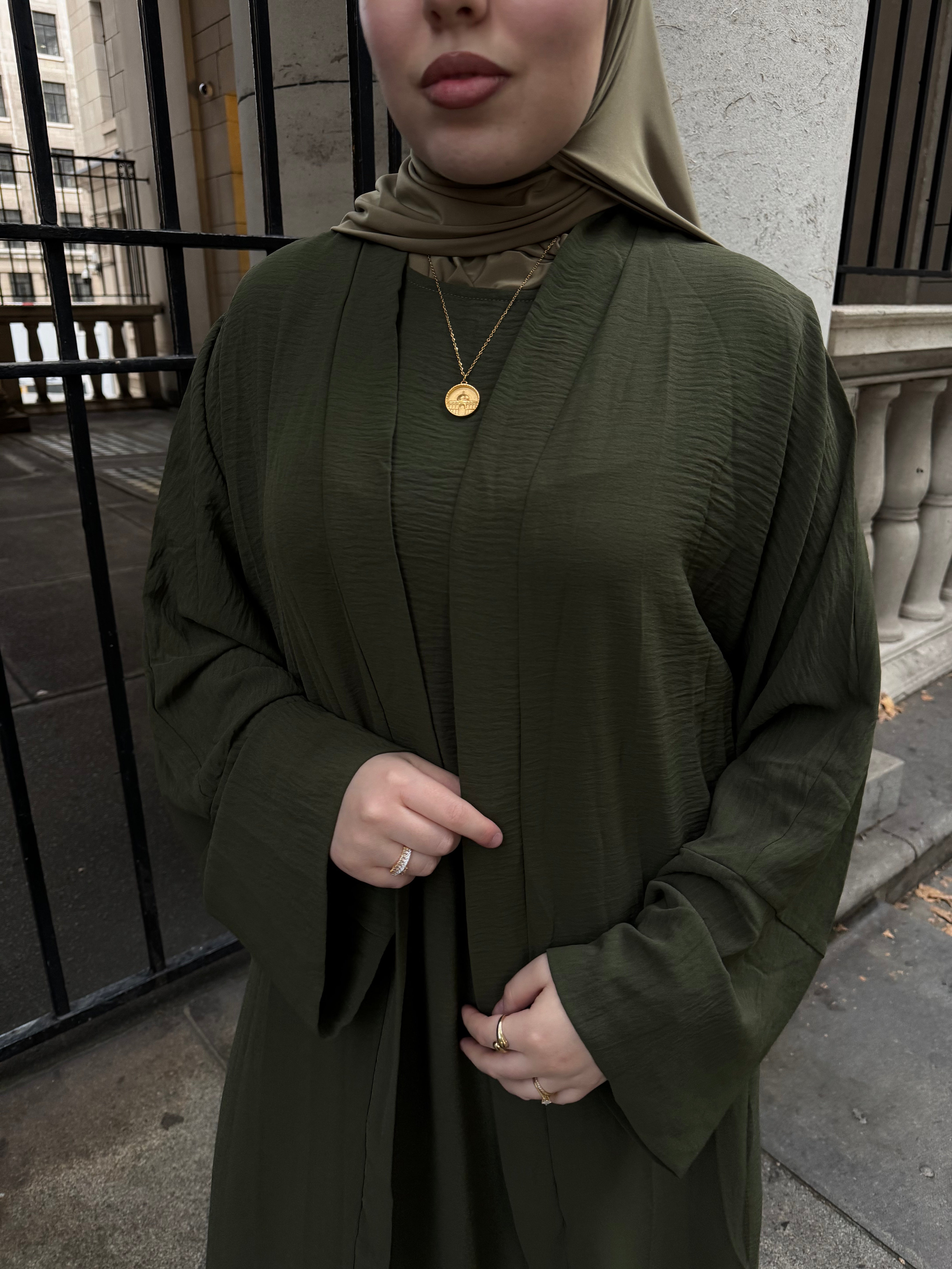 Person wearing a green abaya and headscarf on a city street.