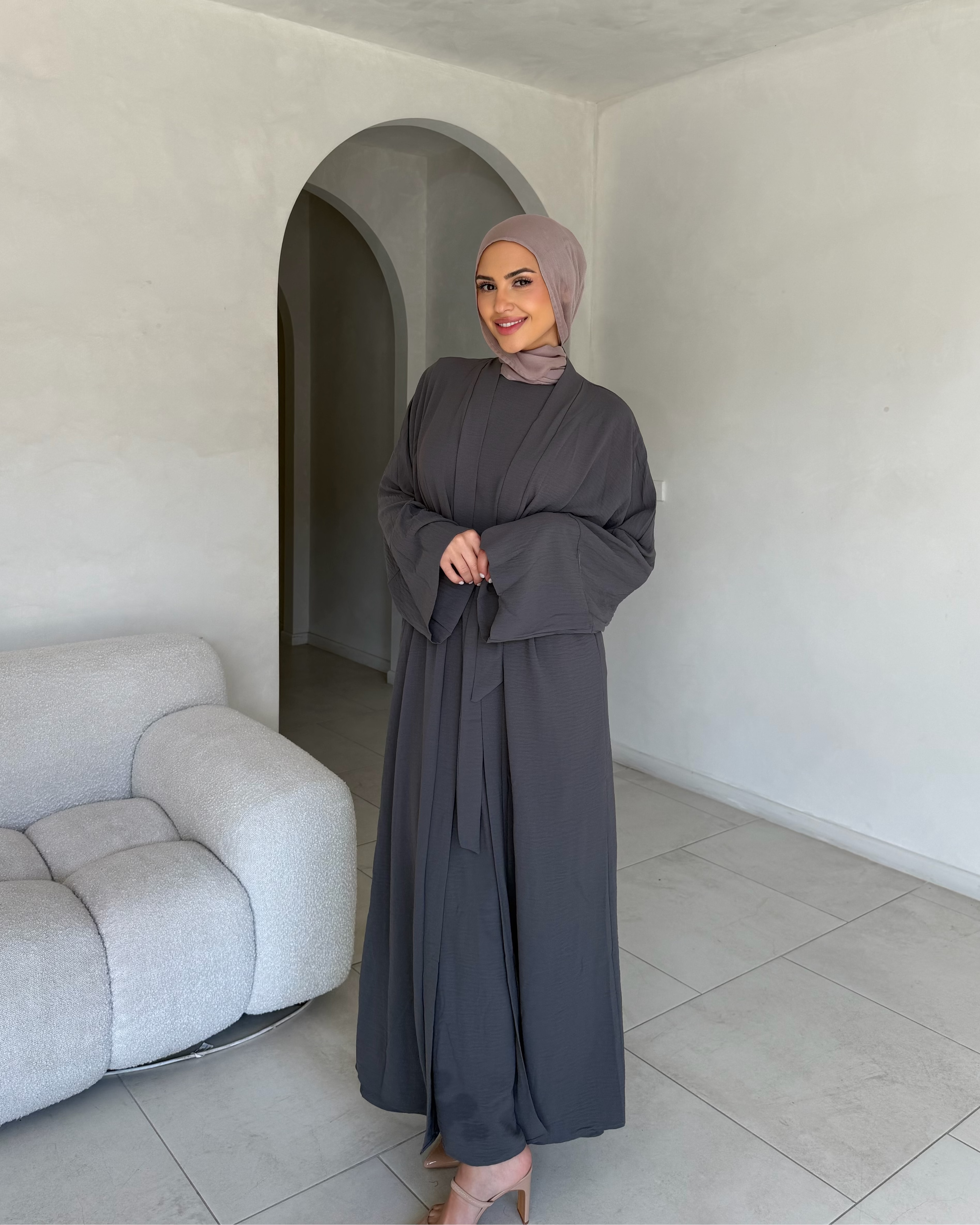 Woman in a gray abaya standing in a modern living room.