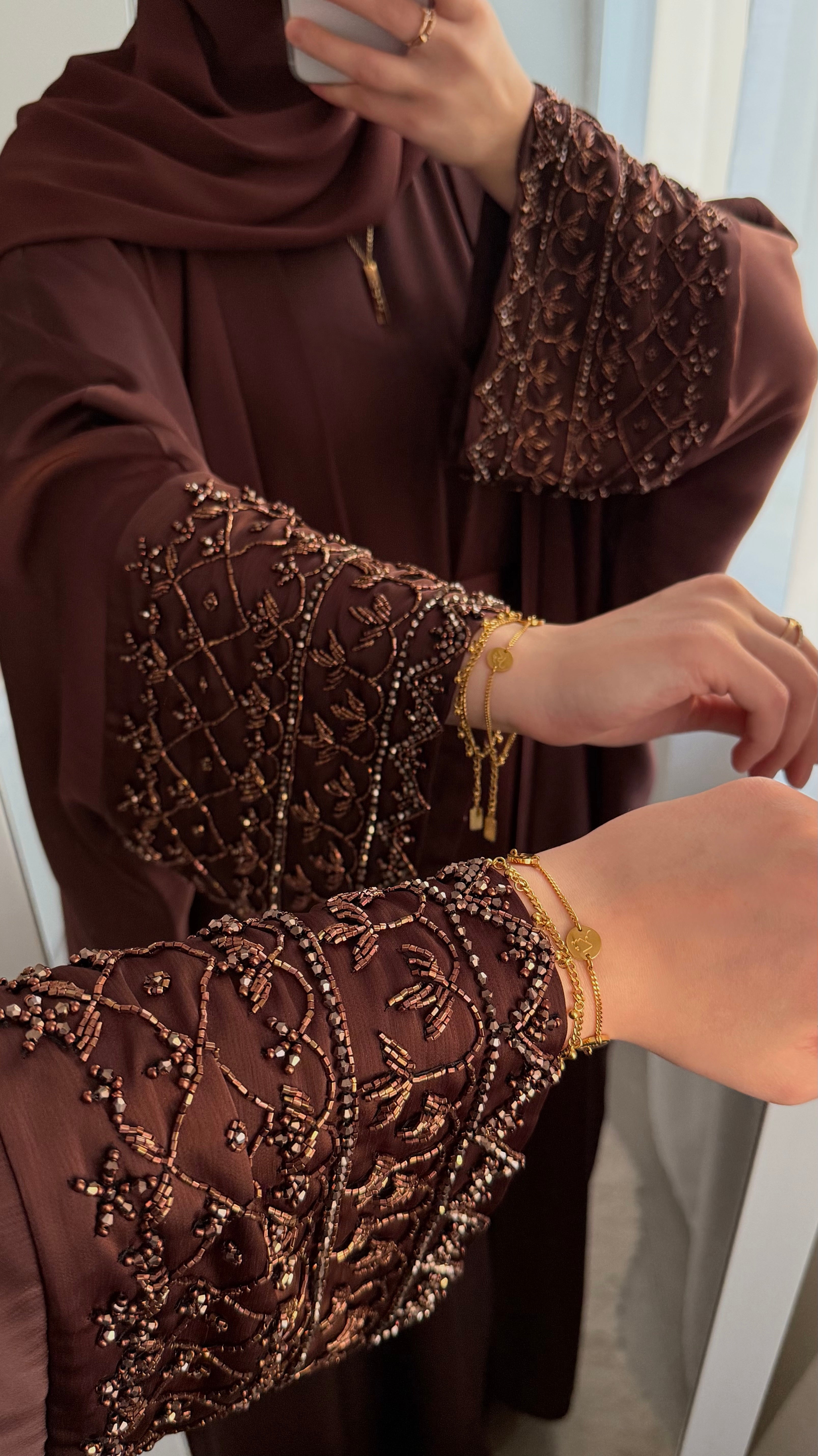 Brown embroidered garment with gold jewelry on a white background