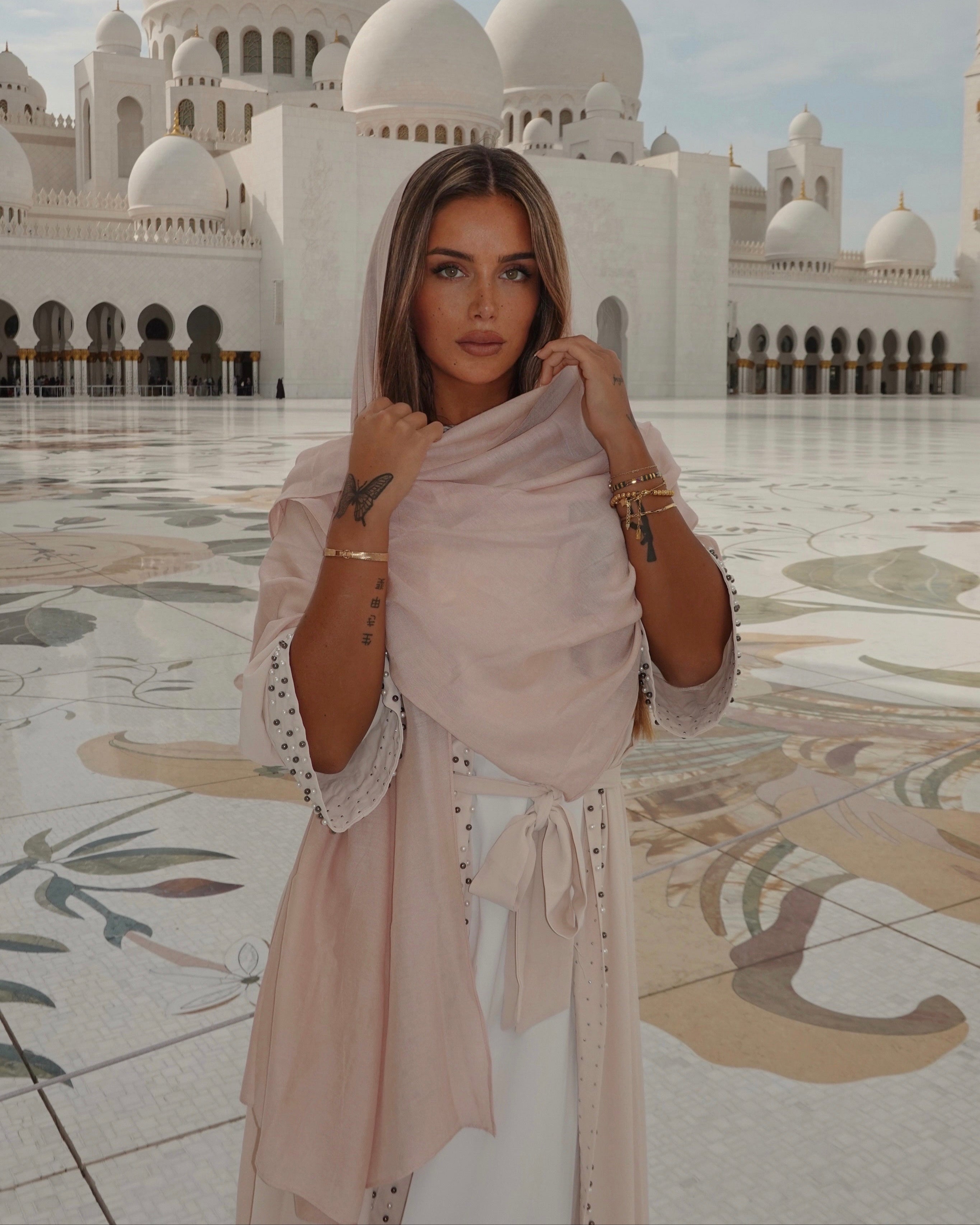 Woman posing in front of a large white mosque with multiple domes.