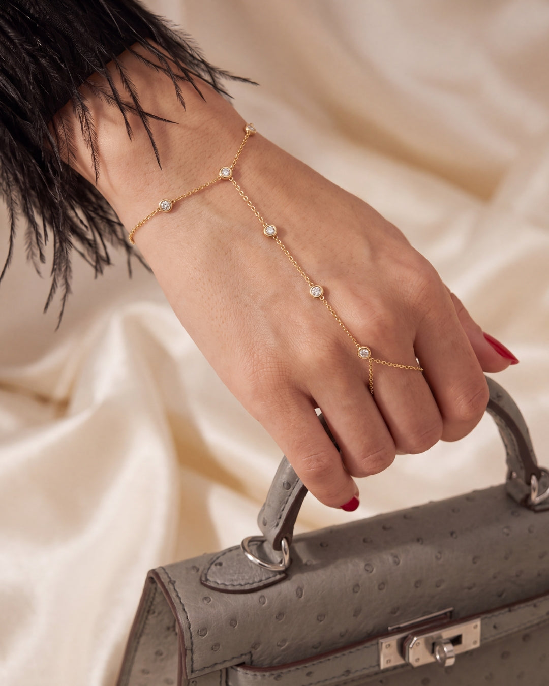 Gold hand chain bracelet with crystals worn on a hand holding a grey leather handbag