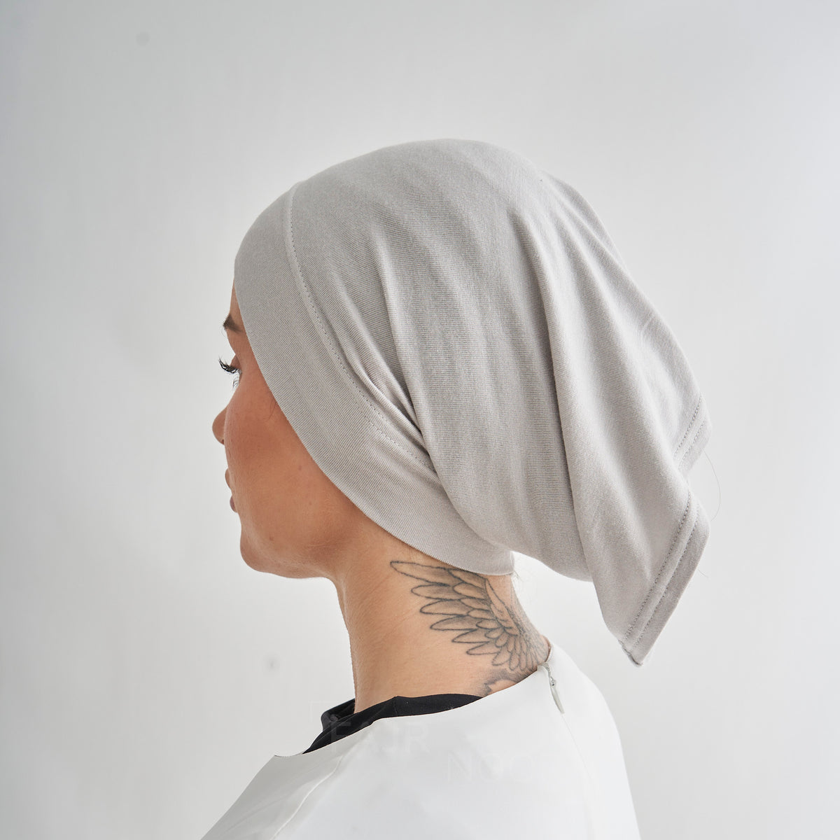 A person shown in side profile wearing a light gray textured fabric head covering or bonnet, with a white salon-style cape visible at the neck against a plain light background.