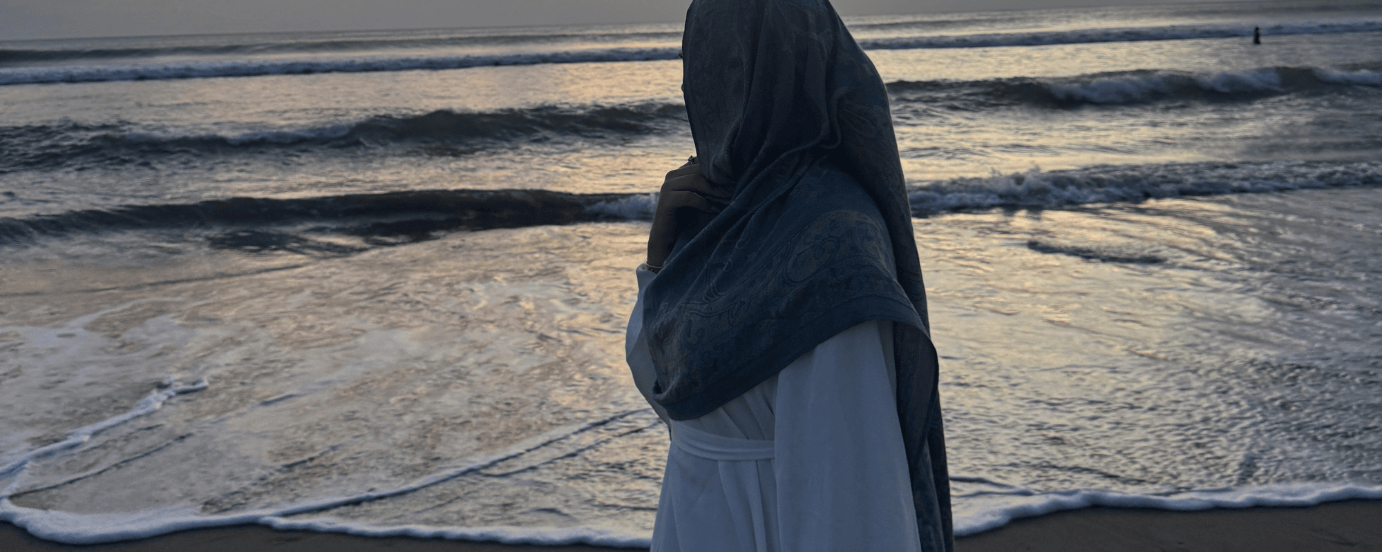 Person wearing a hijab standing on a beach with waves in the background