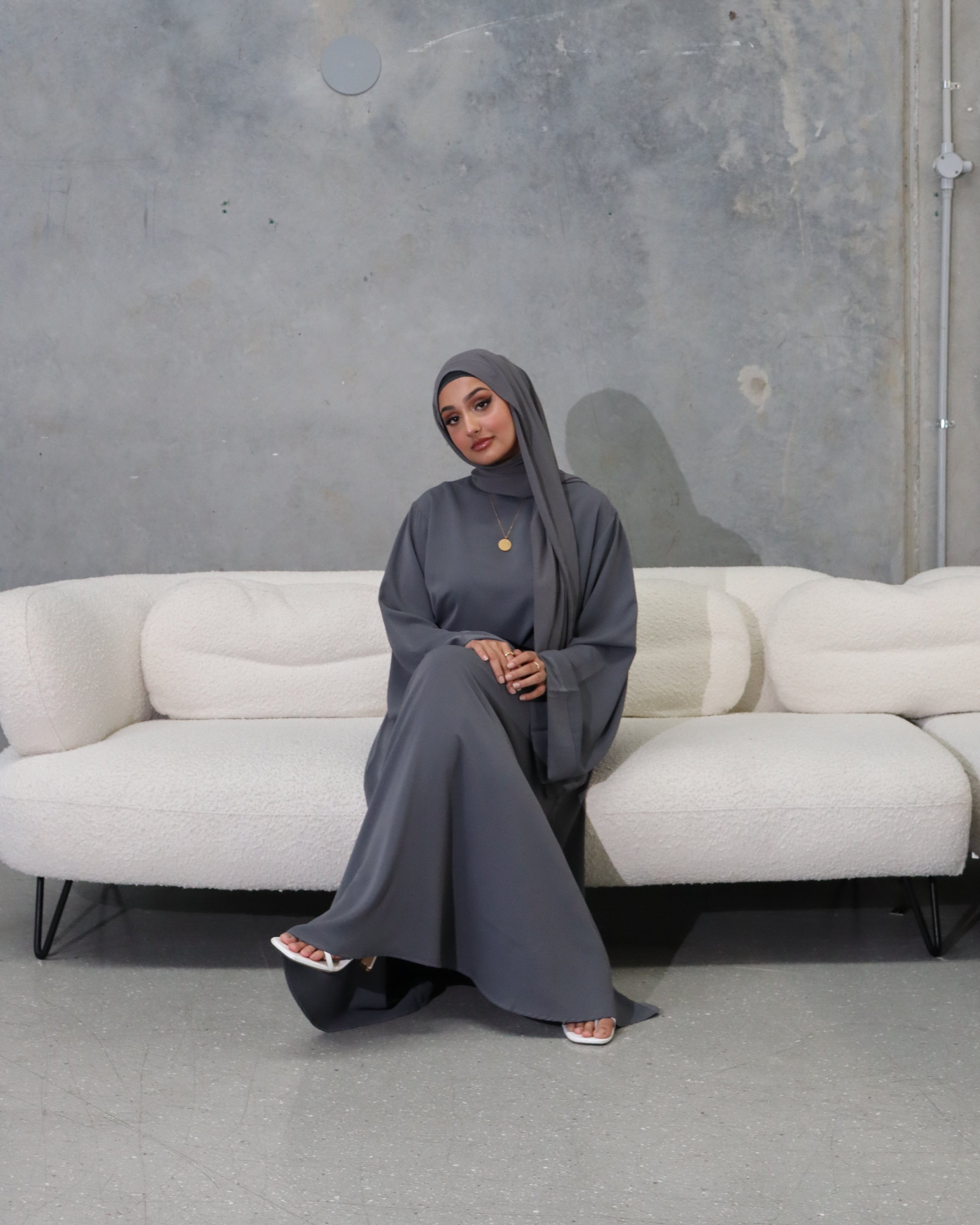 Person wearing a dark gray outfit sitting on a white bench in an urban setting.
