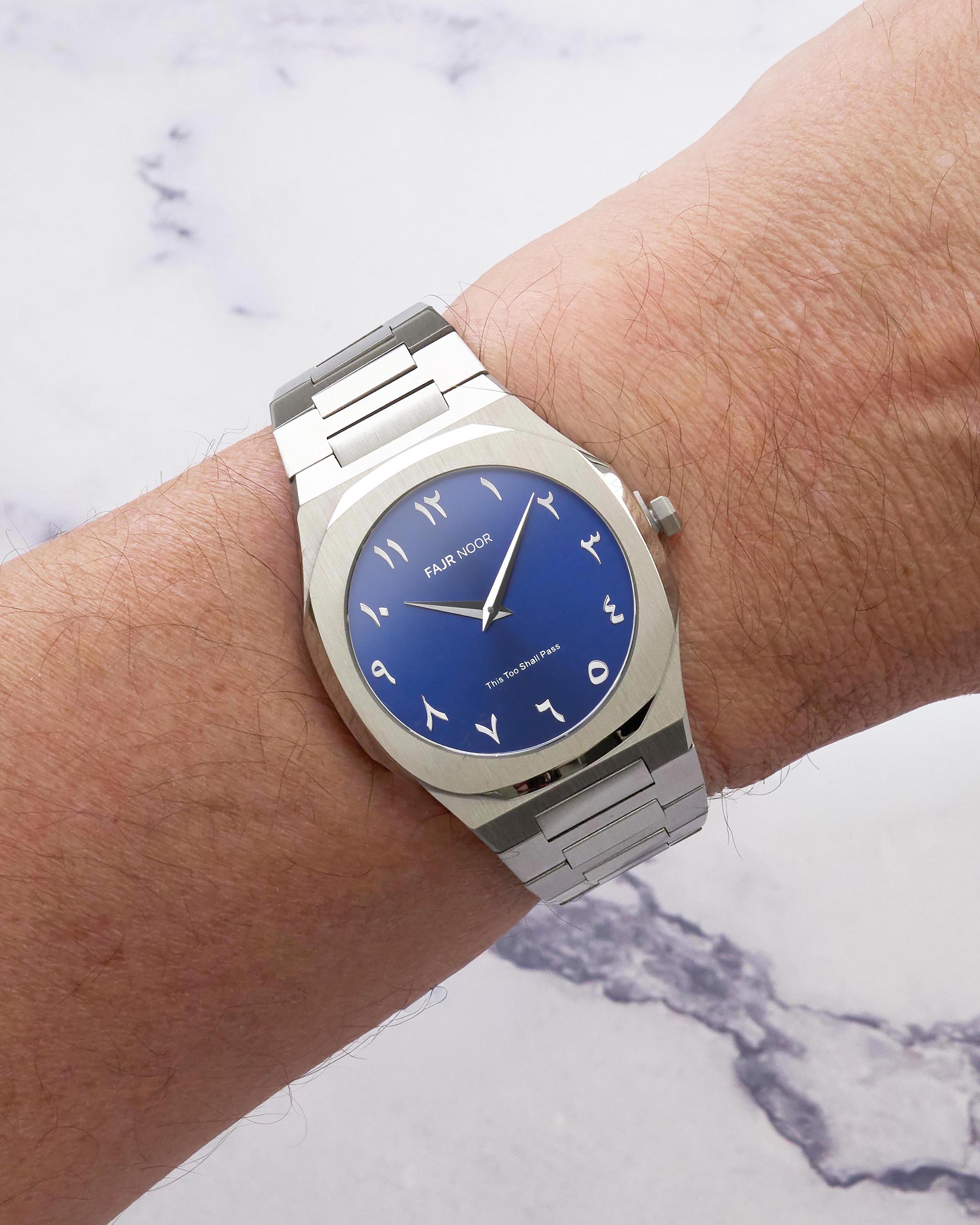 Silver watch with a blue dial on a wrist against a marble background