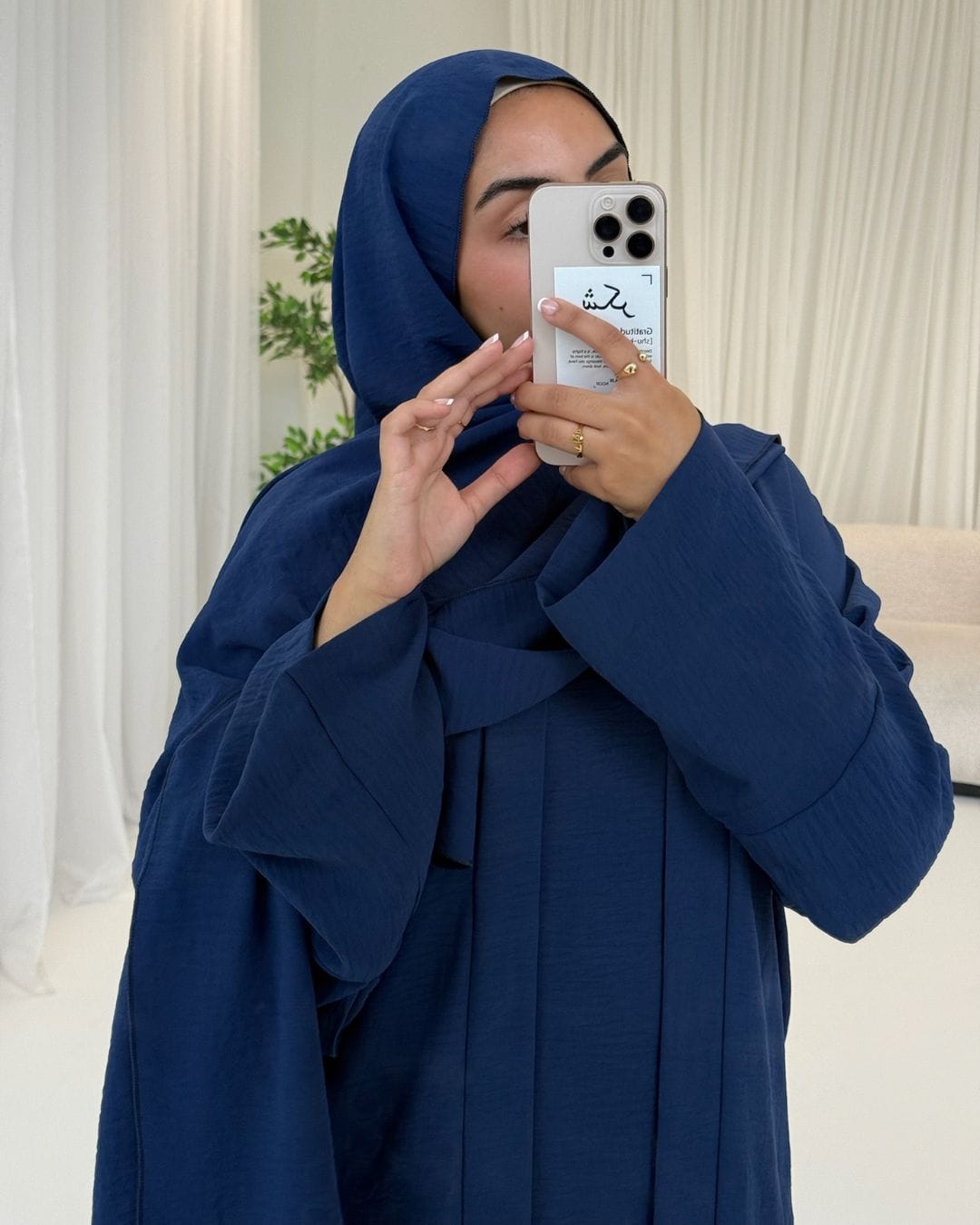 Person wearing a blue hijab and coat, holding a phone with a white background