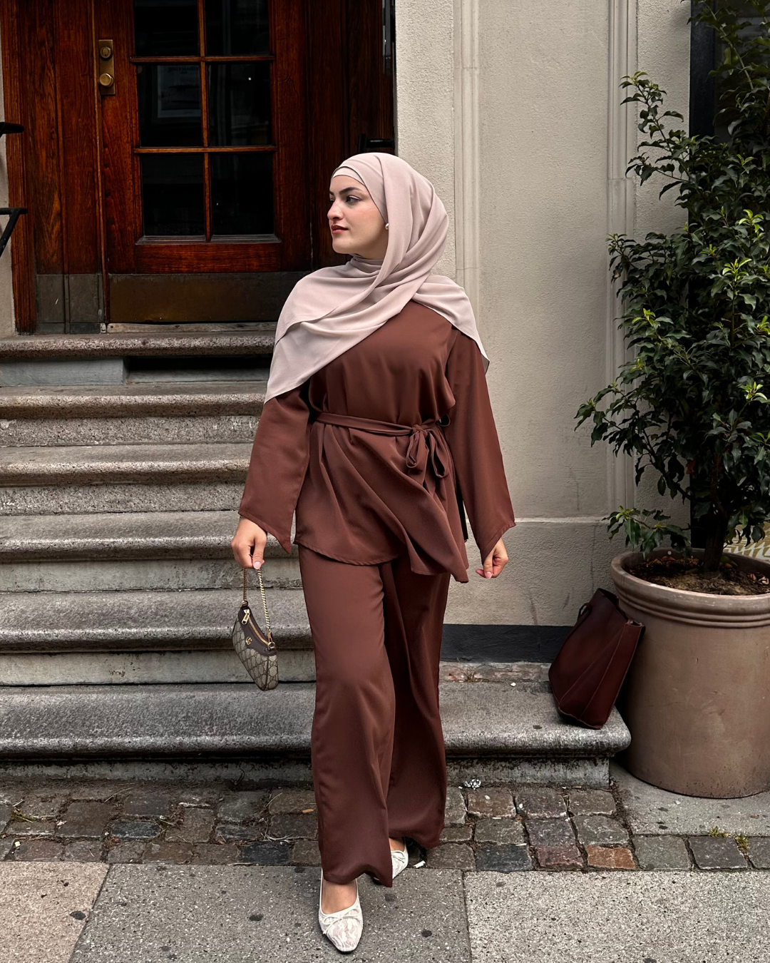 Woman in a brown outfit standing on steps outside a building