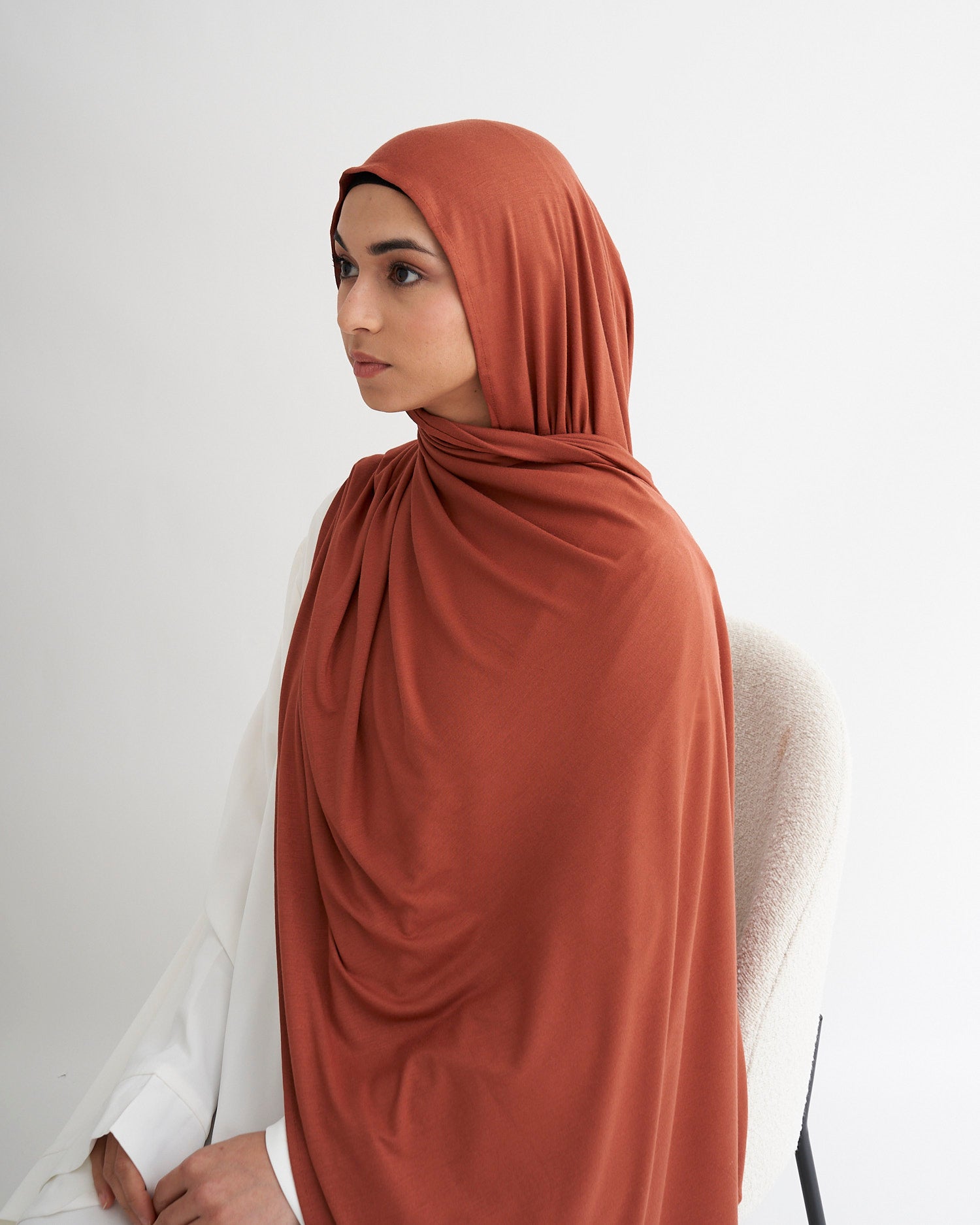 Woman wearing a rust-colored hijab against a white background