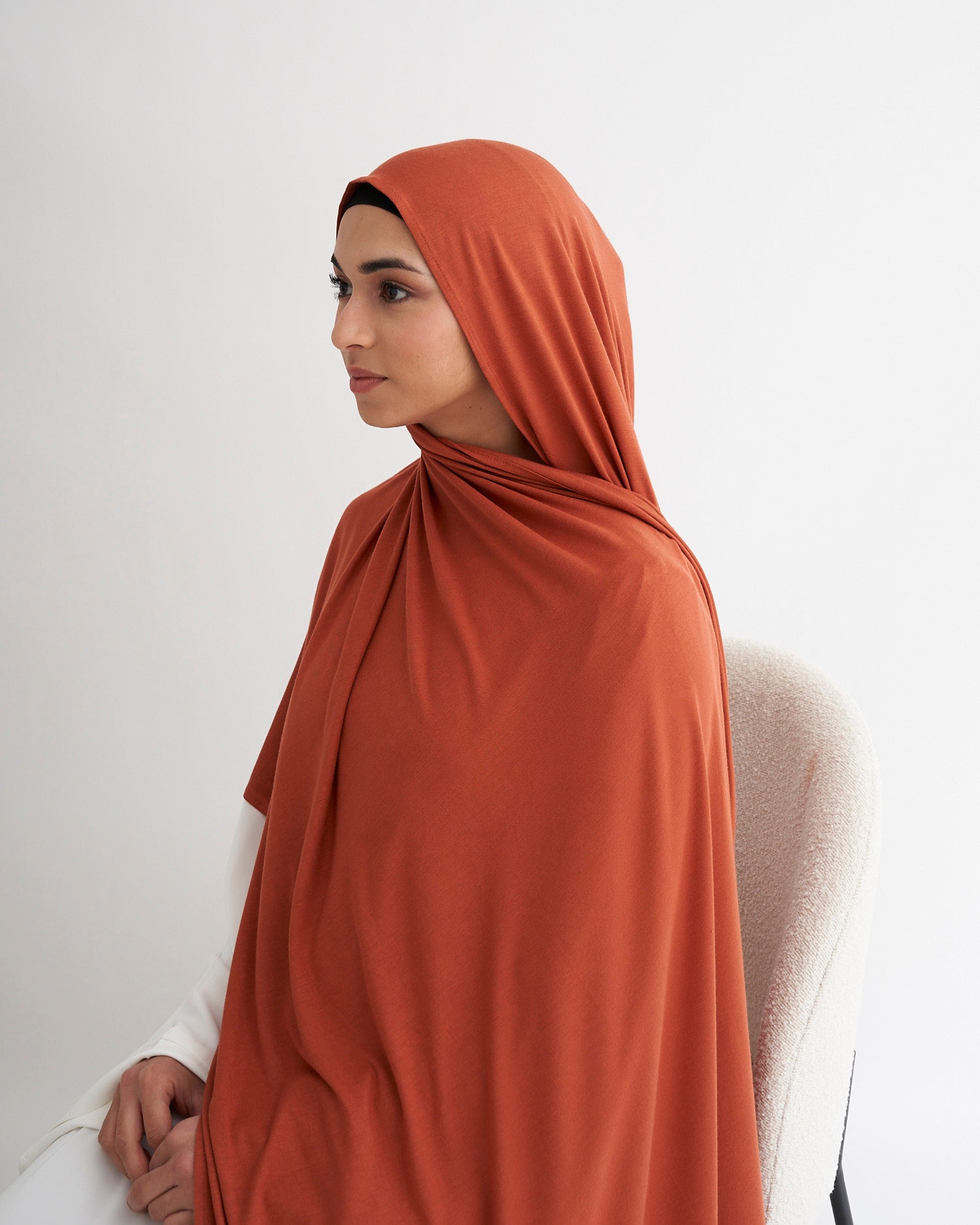 Woman wearing a rust-colored hijab against a white background