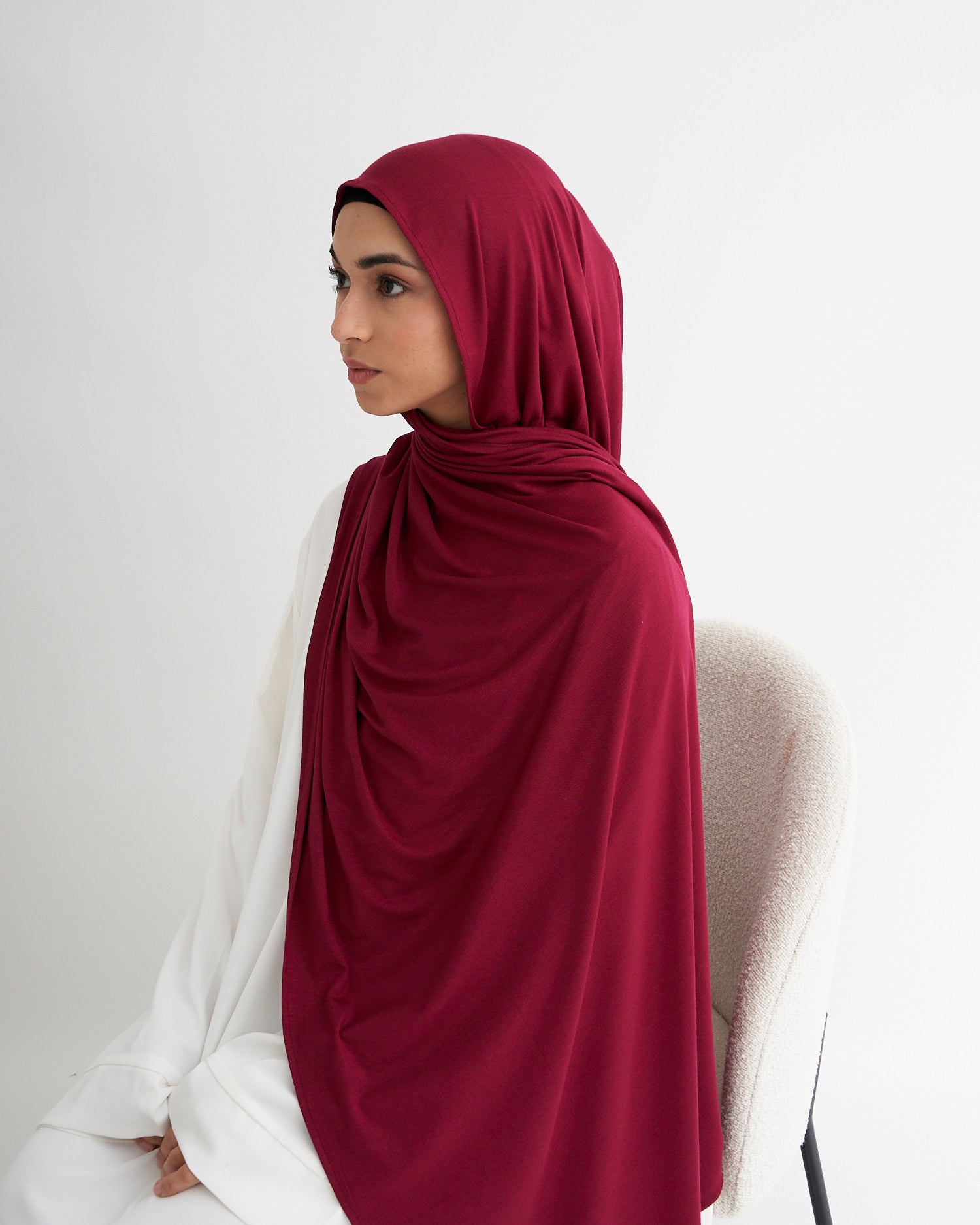 Woman wearing a burgundy hijab and white outfit against a plain background