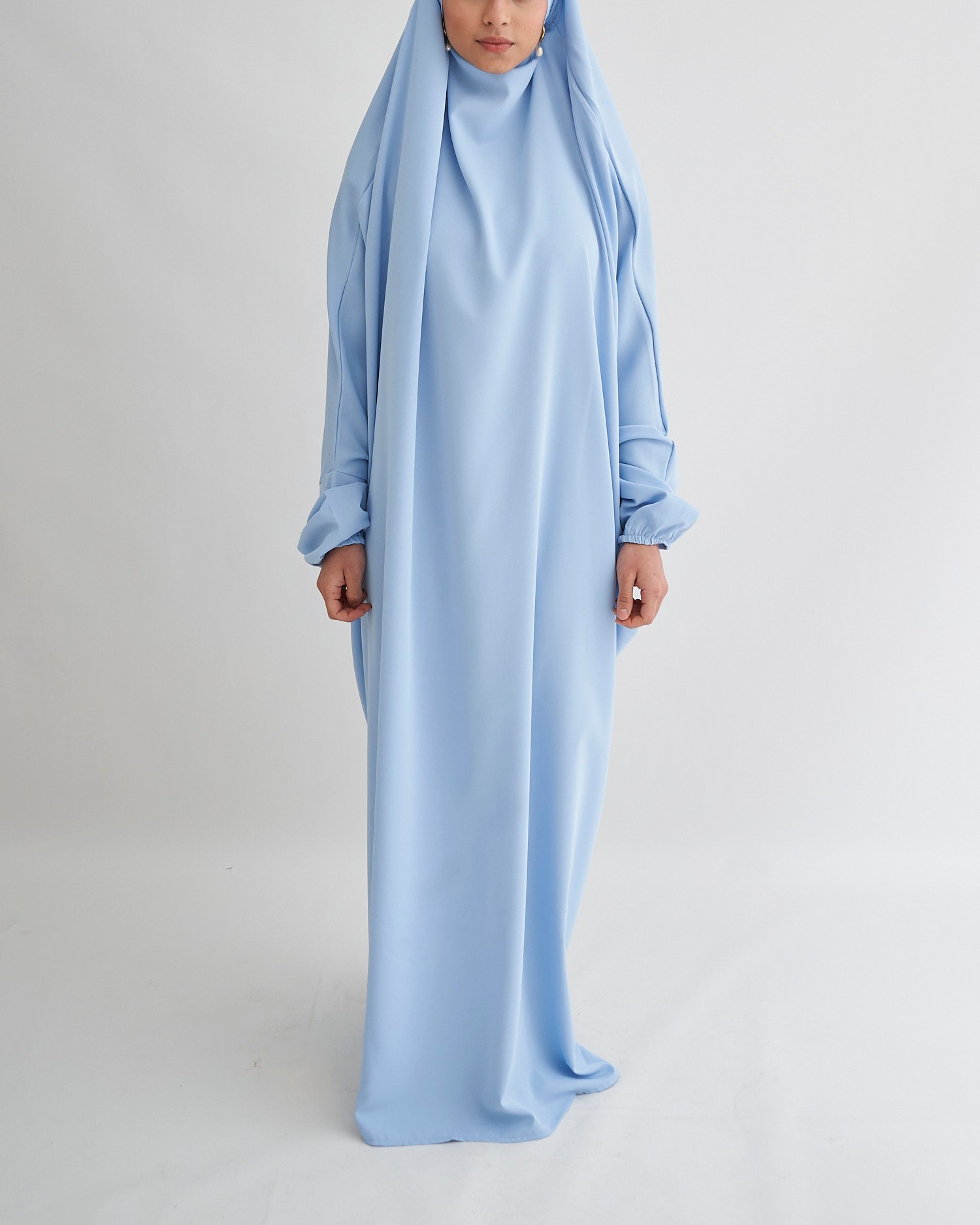 Person wearing a light blue abaya on a plain background