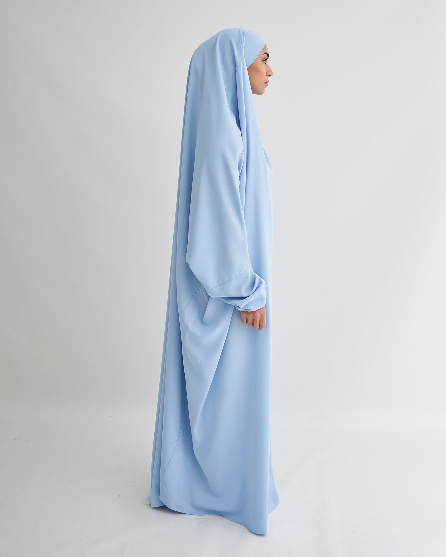 Woman wearing a light blue abaya against a plain background