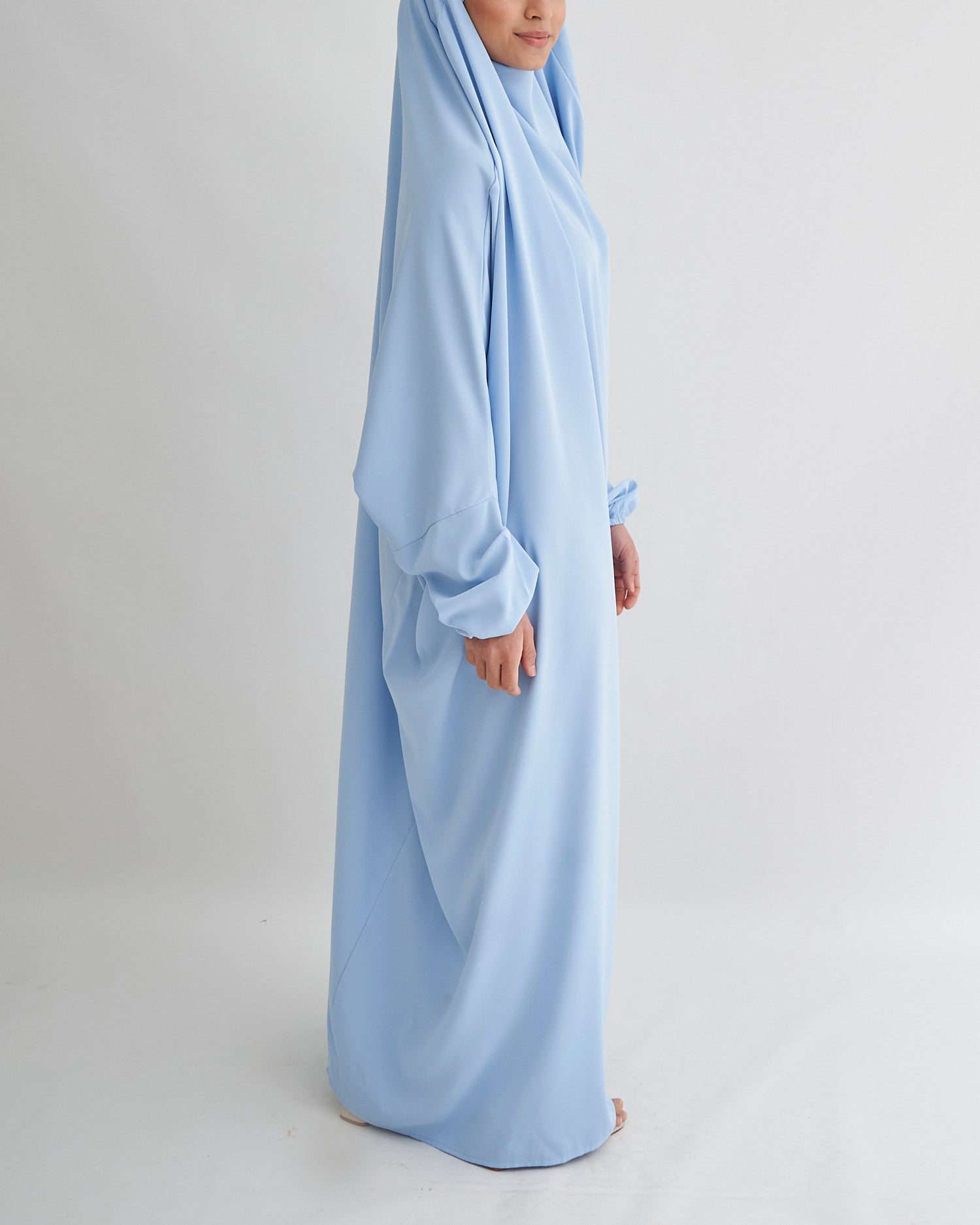Person wearing a light blue abaya on a plain background