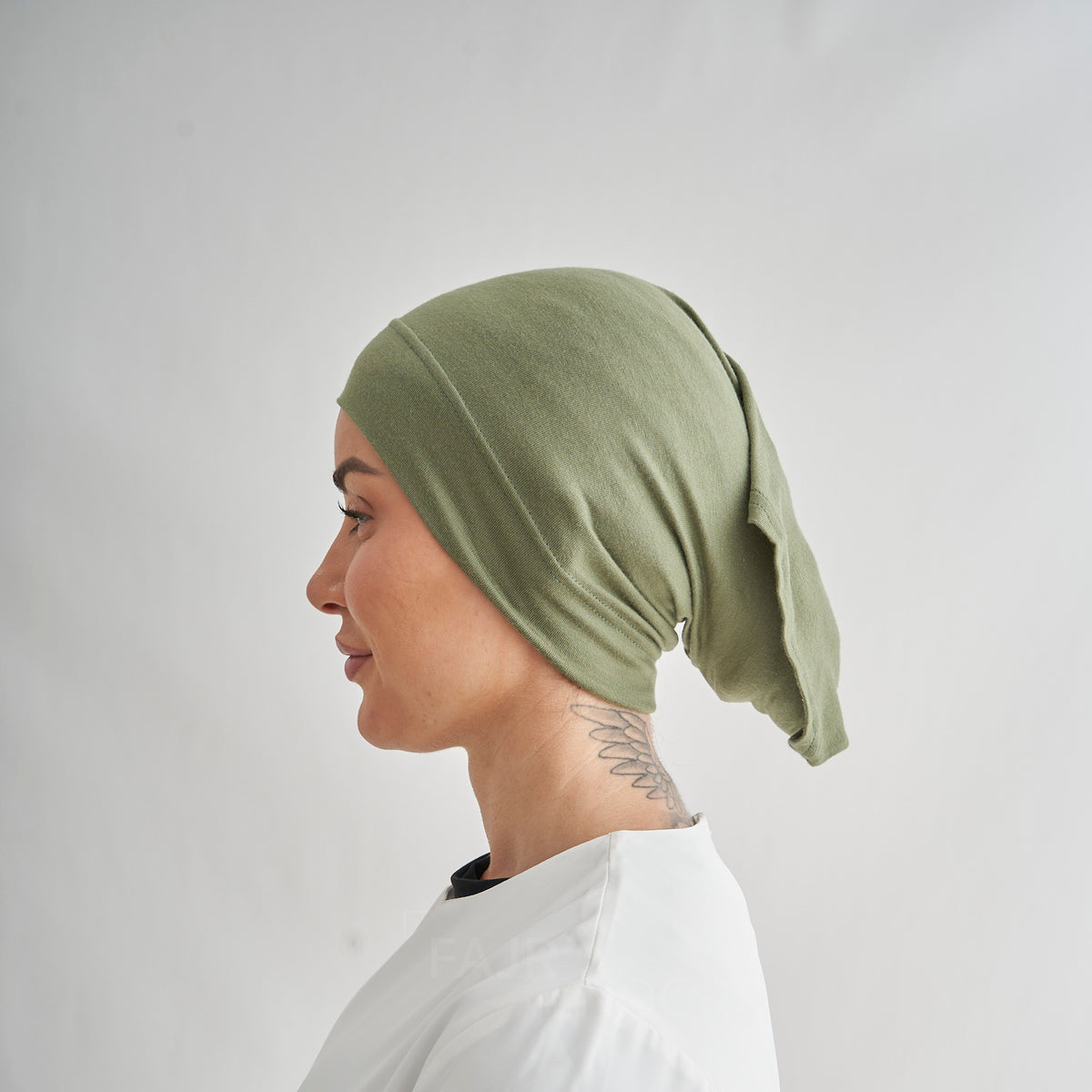 A side-profile view of a person wearing an olive green fabric head covering, set against a plain light gray background.