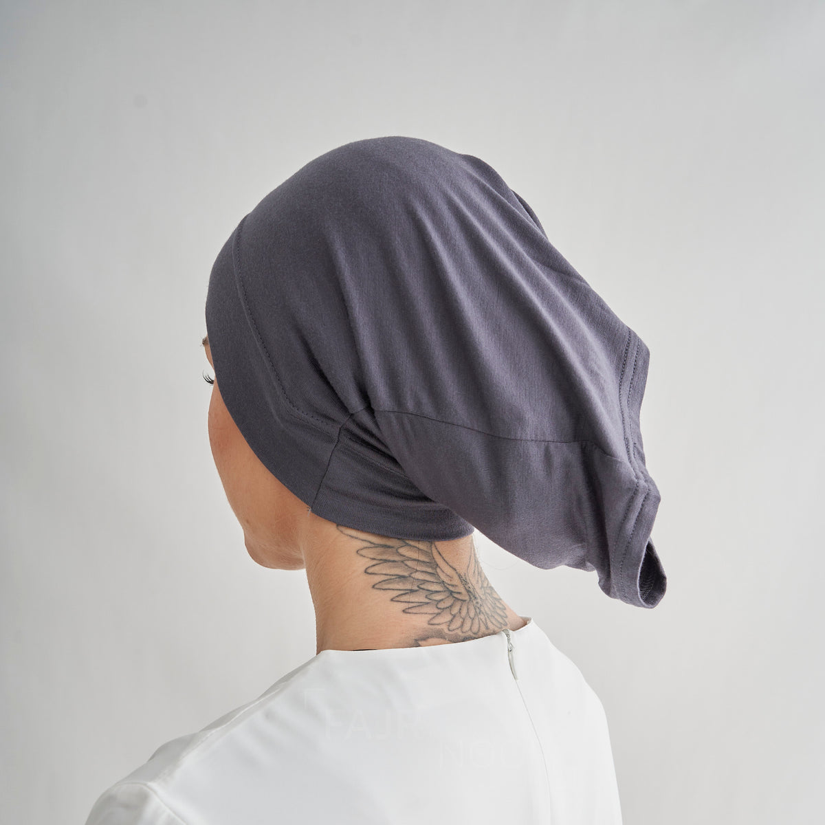 A person shown from the back wearing a dark gray fabric head covering or hijab, against a plain light gray background.