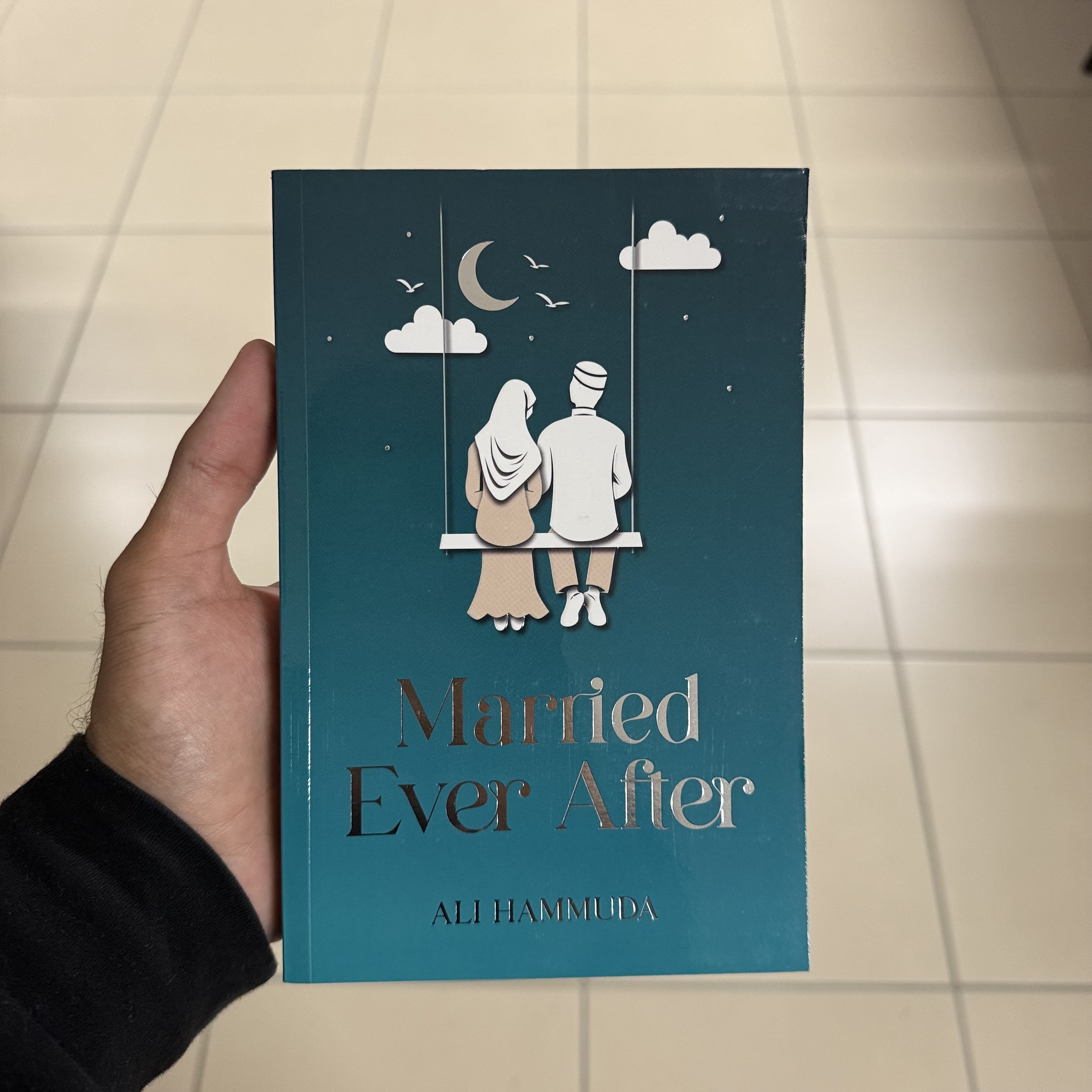 Book titled 'Married Ever After' held by a hand on a tiled floor.