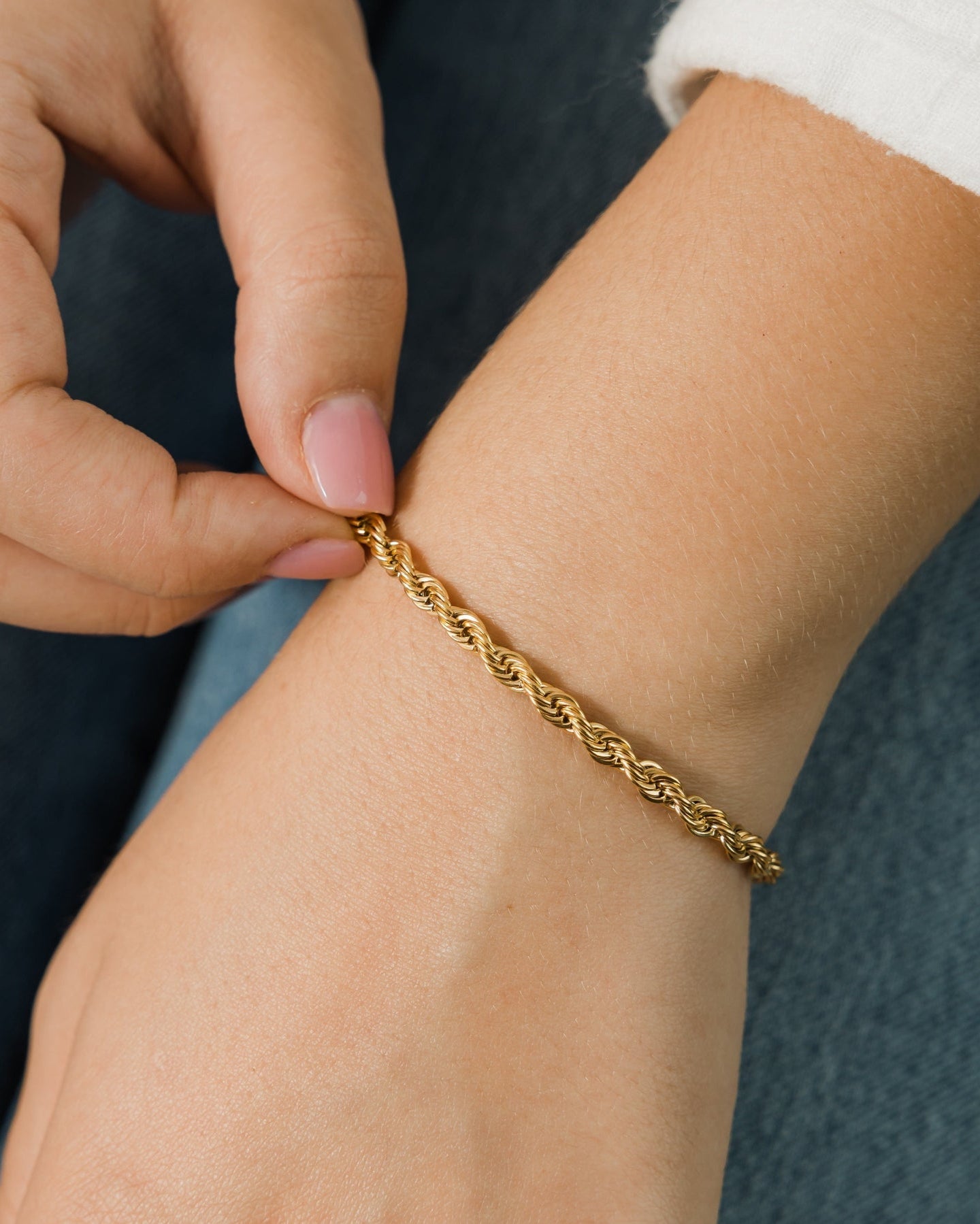 Gold bracelet being adjusted on a wrist against a neutral background