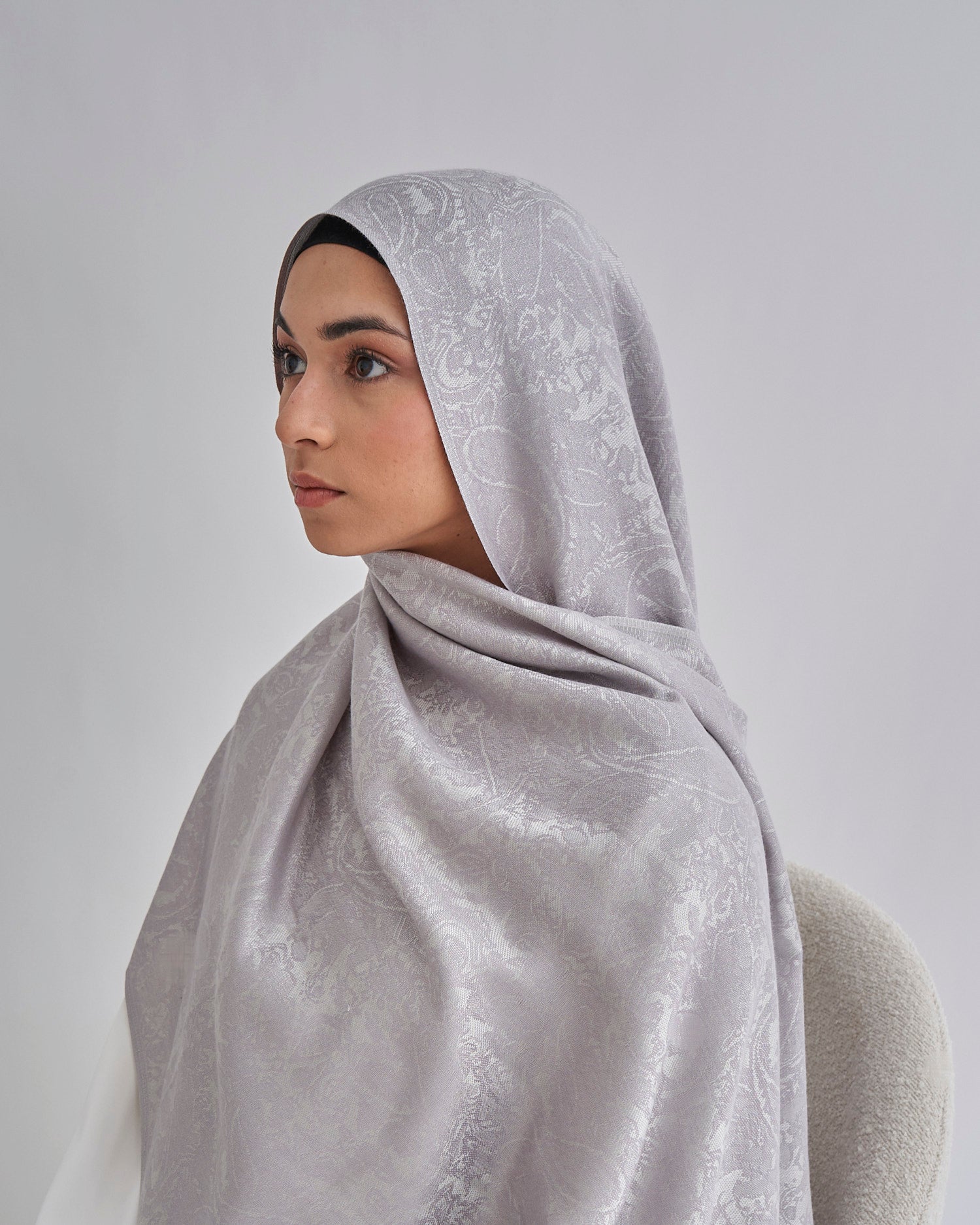 Woman wearing a gray hijab with lace details against a plain background