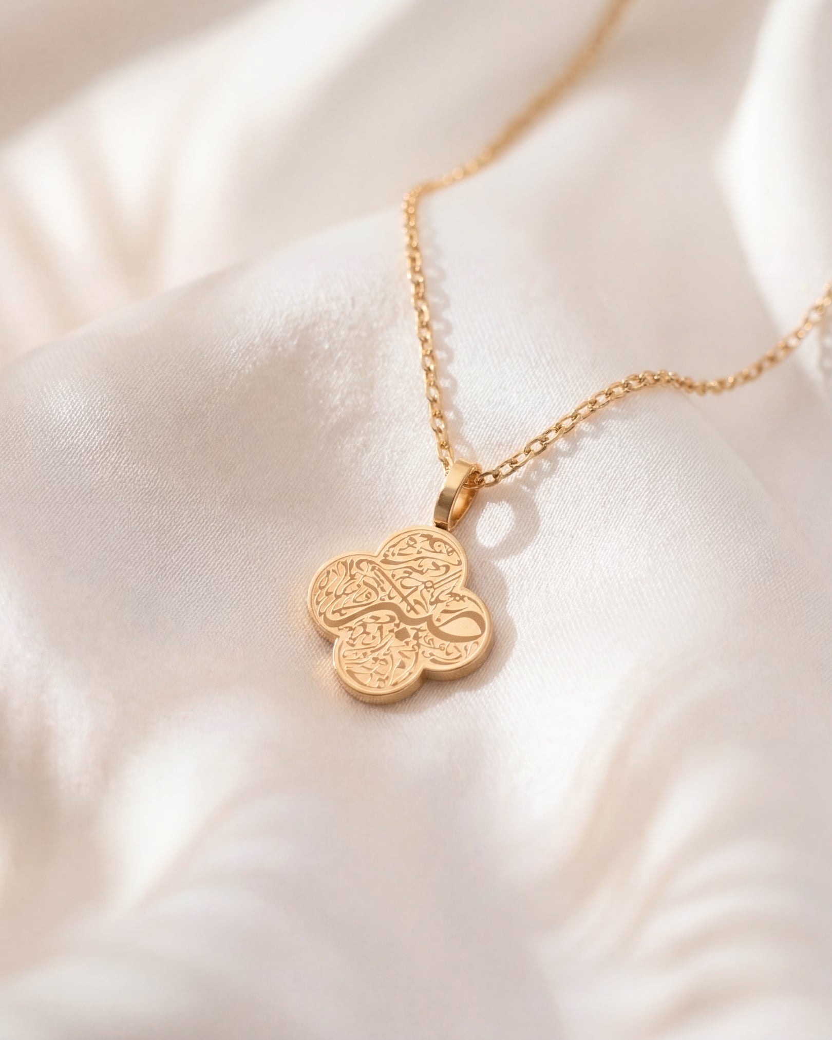 Gold necklace with a clover-shaped pendant on a white fabric background