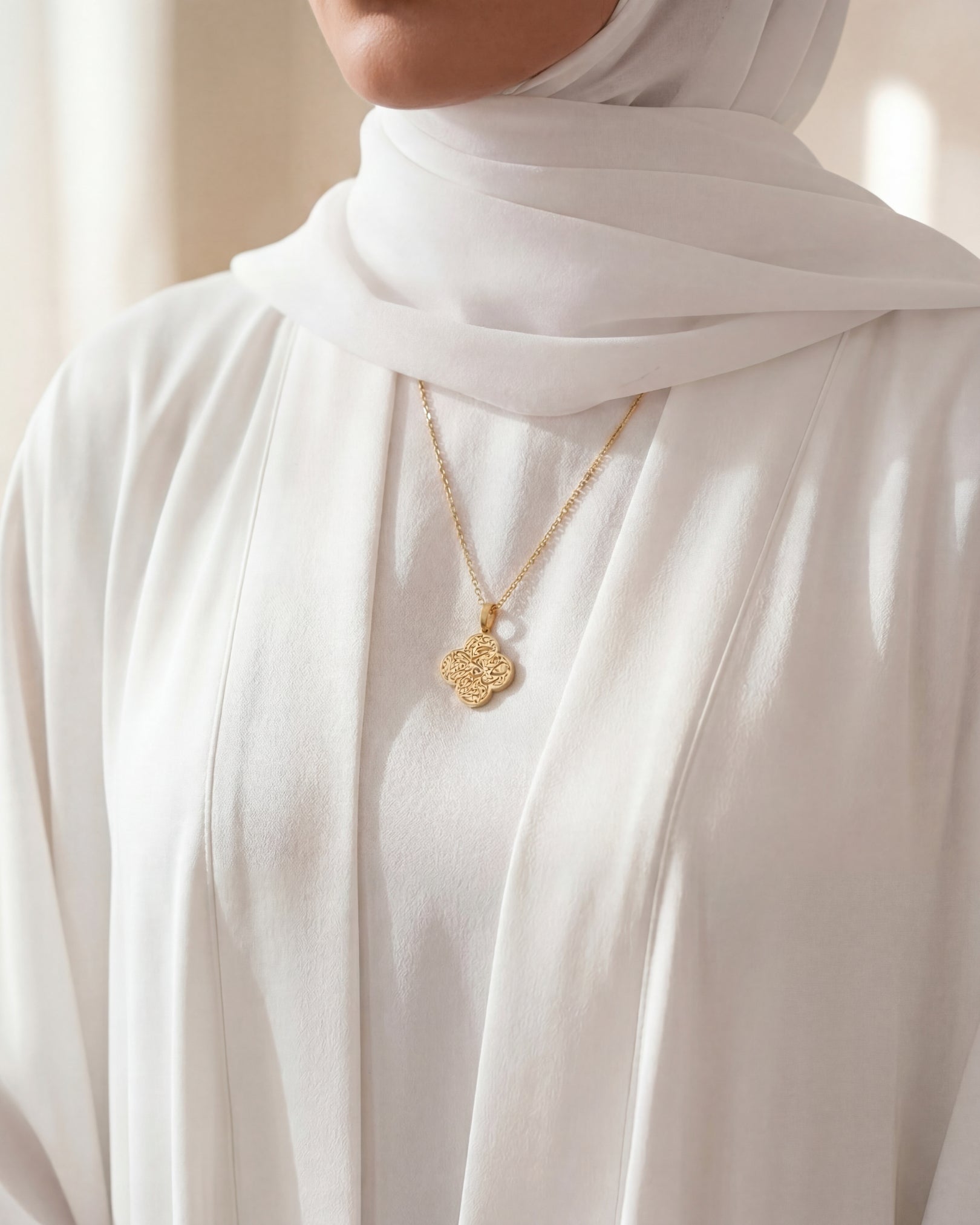 Person wearing a gold necklace with a white hijab