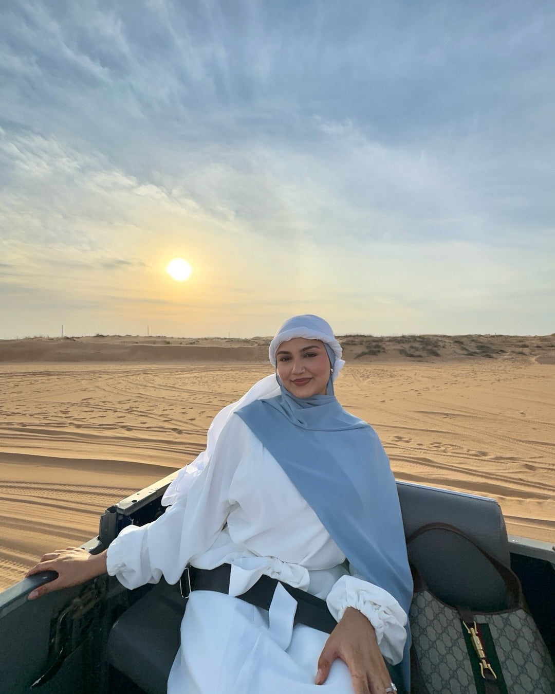 Woman in a hijab sitting in an open vehicle in a desert with a sunset.