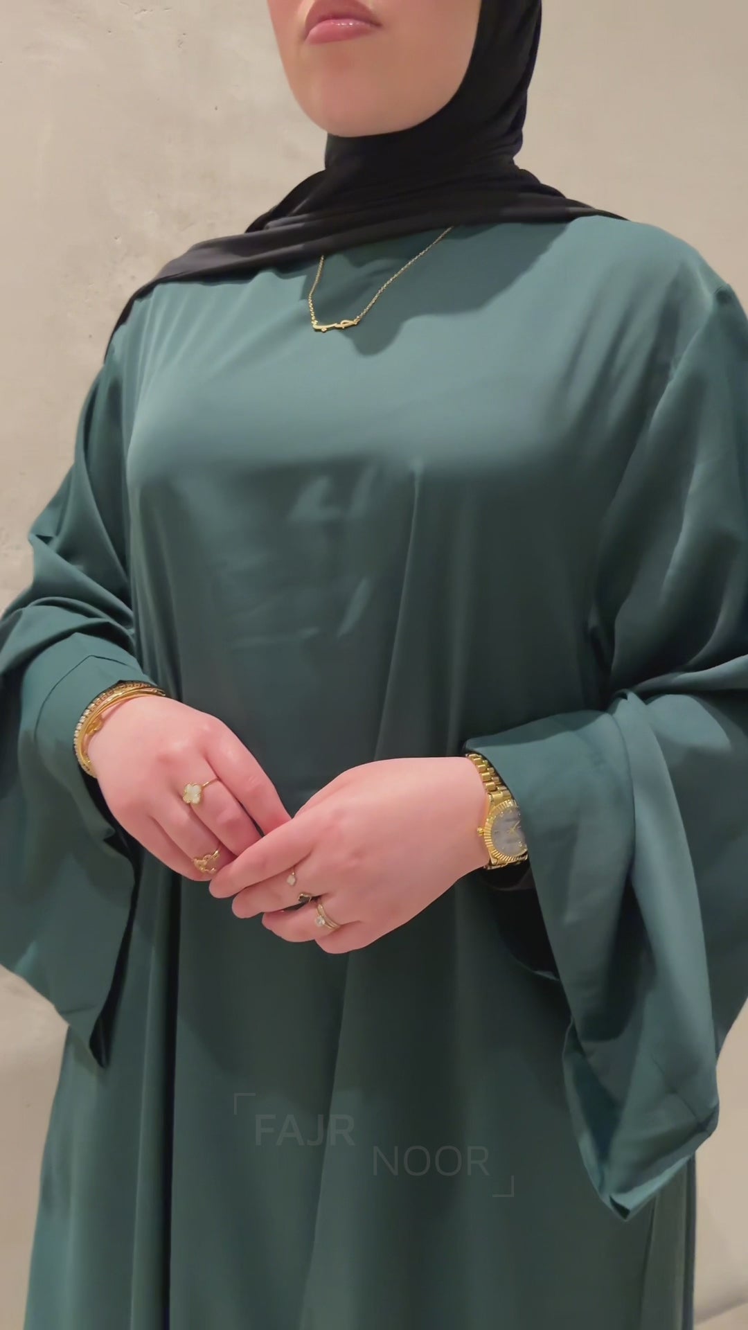 Close-up of a woman wearing the Fajr Noor Khatijah Abaya in emerald, showing gold jewelry and the Arabic Hub Love necklace