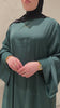 Close-up of a woman wearing the Fajr Noor Khatijah Abaya in emerald, showing gold jewelry and the Arabic Hub Love necklace