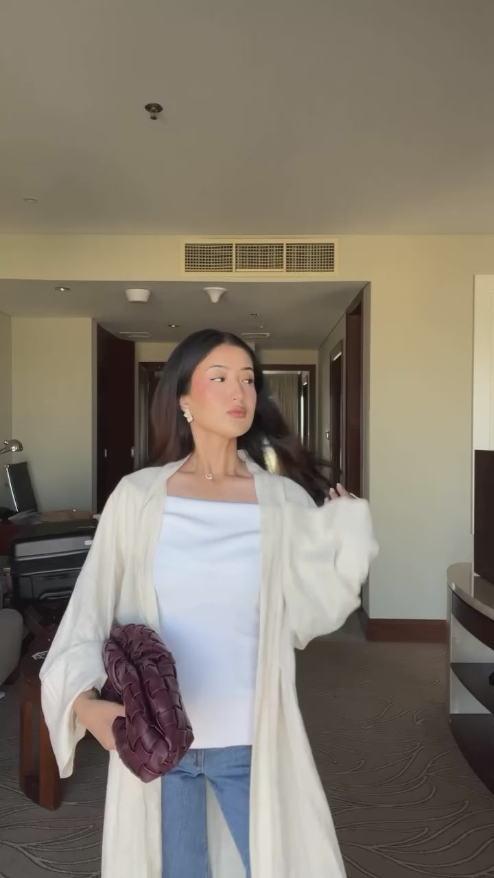 Woman wearing the Fajr Noor Aya Linen open abaya in sand, styled over jeans and a white top