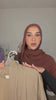 Woman wearing the Fajr Noor Aya Linen Abaya in coffee brown with a matching hijab, trying on a khaki abaya from her wardrobe