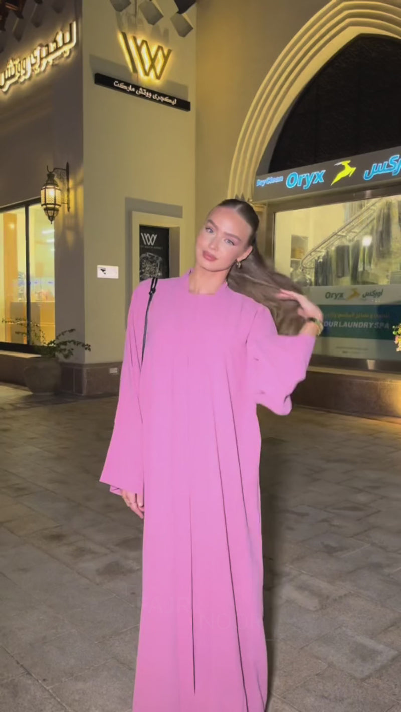 Woman wearing the Fajr Noor Crinkle Abaya in bright pink, standing on an evening street
