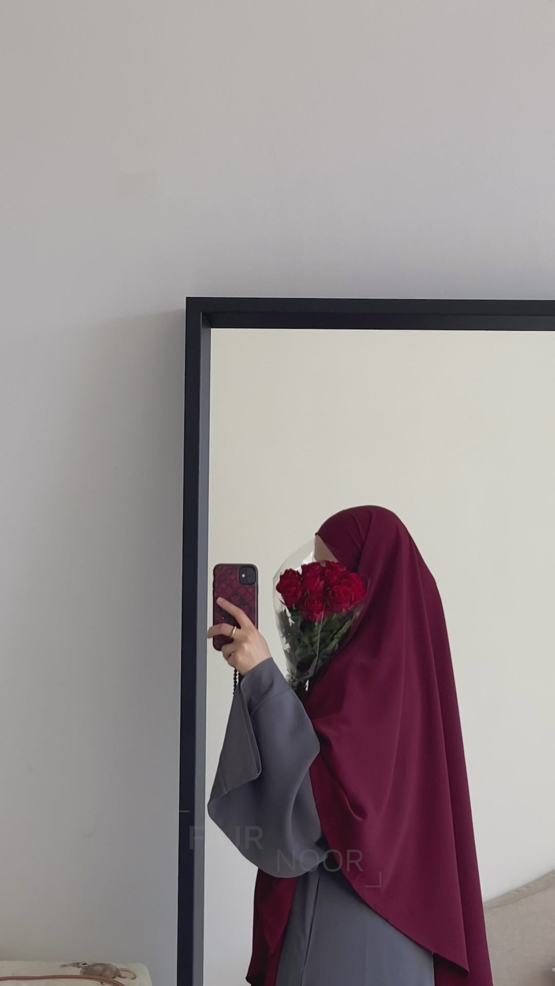 Woman wearing the Fajr Noor Khatijah Abaya in charcoal with a maroon khimar, holding red roses in a mirror selfie