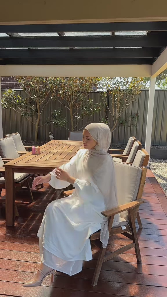 Woman wearing the Fajr Noor Essential Cuffed Abaya in white with a matching hijab, sitting outdoors