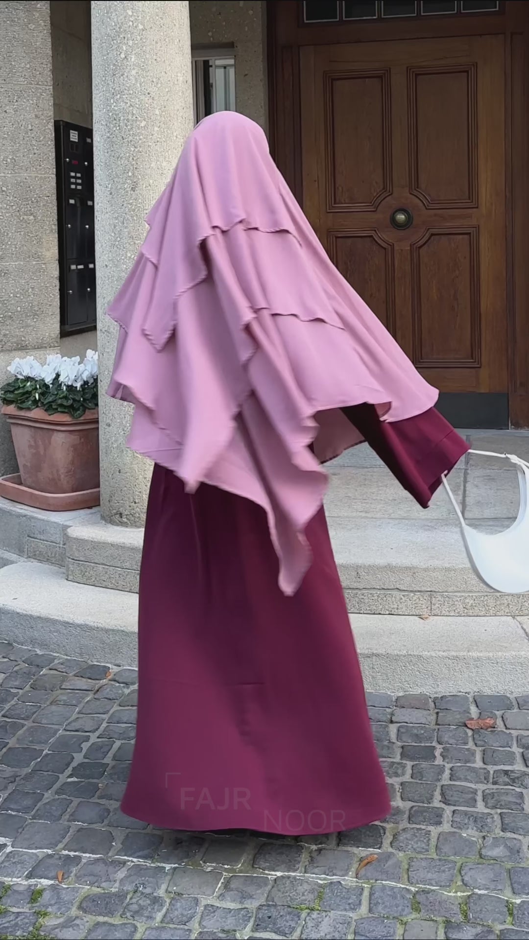 Woman wearing the Fajr Noor Khatijah Abaya in maroon with a berry chiffon khimar, walking outdoors