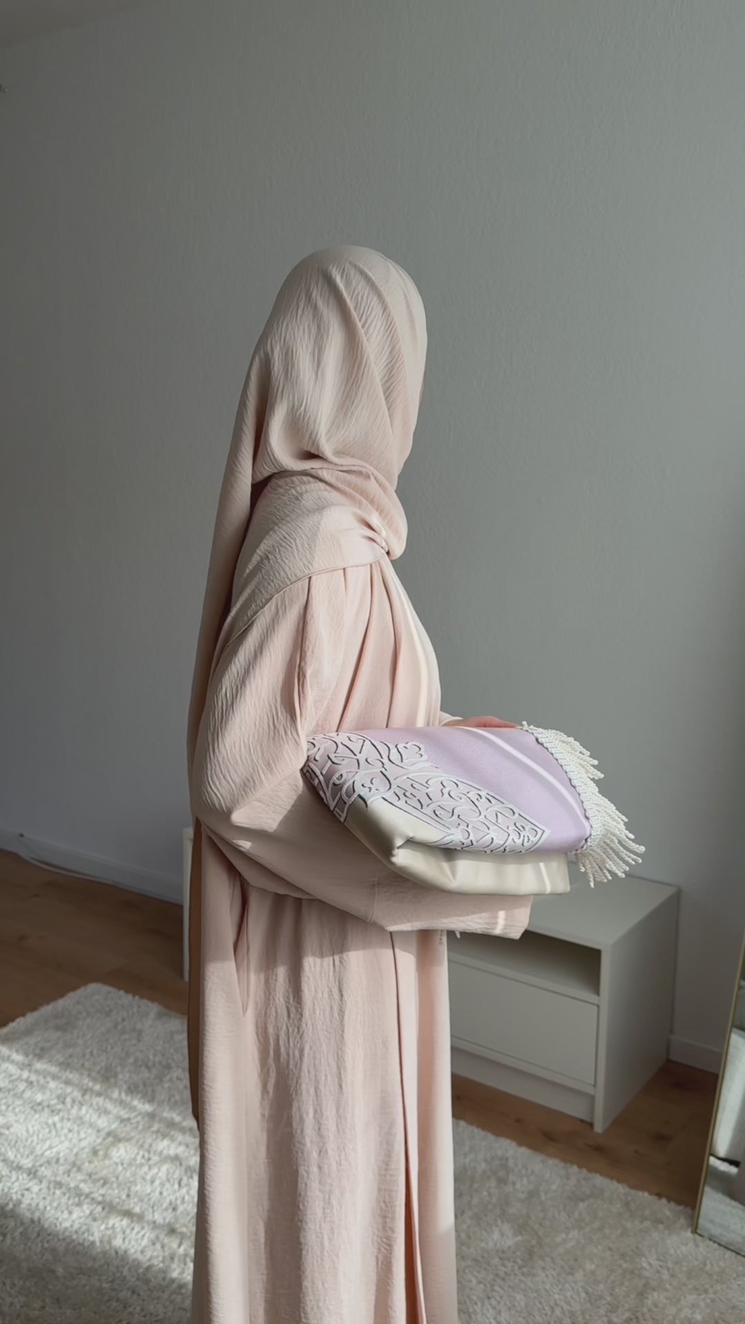 Woman wearing the Fajr Noor Crinkle Abaya in cream, fully covered, holding a decorative prayer mat