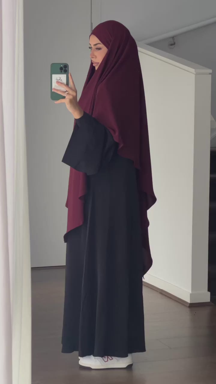 Woman wearing the Fajr Noor Khatijah Abaya in navy with a maroon khimar, taking a mirror selfie