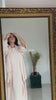 Woman wearing the Fajr Noor Crinkle Abaya in cream, reflected in an ornate mirror, styling her hijab
