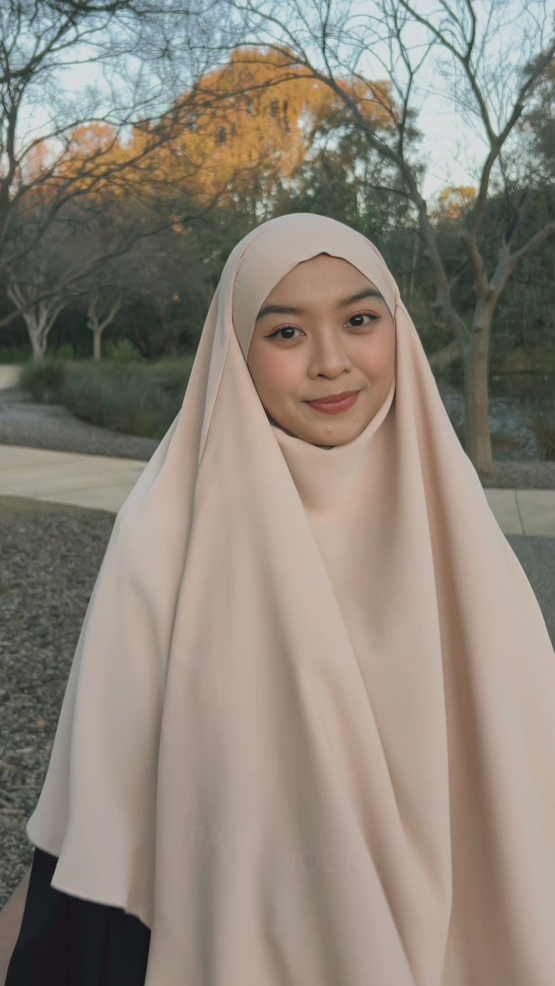 Woman wearing the Fajr Noor Khatijah Abaya in black with a cream khimar, outdoors in a park
