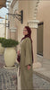 Woman wearing the Fajr Noor Aya Linen Abaya in khaki with a maroon hijab, walking outdoors near an archway