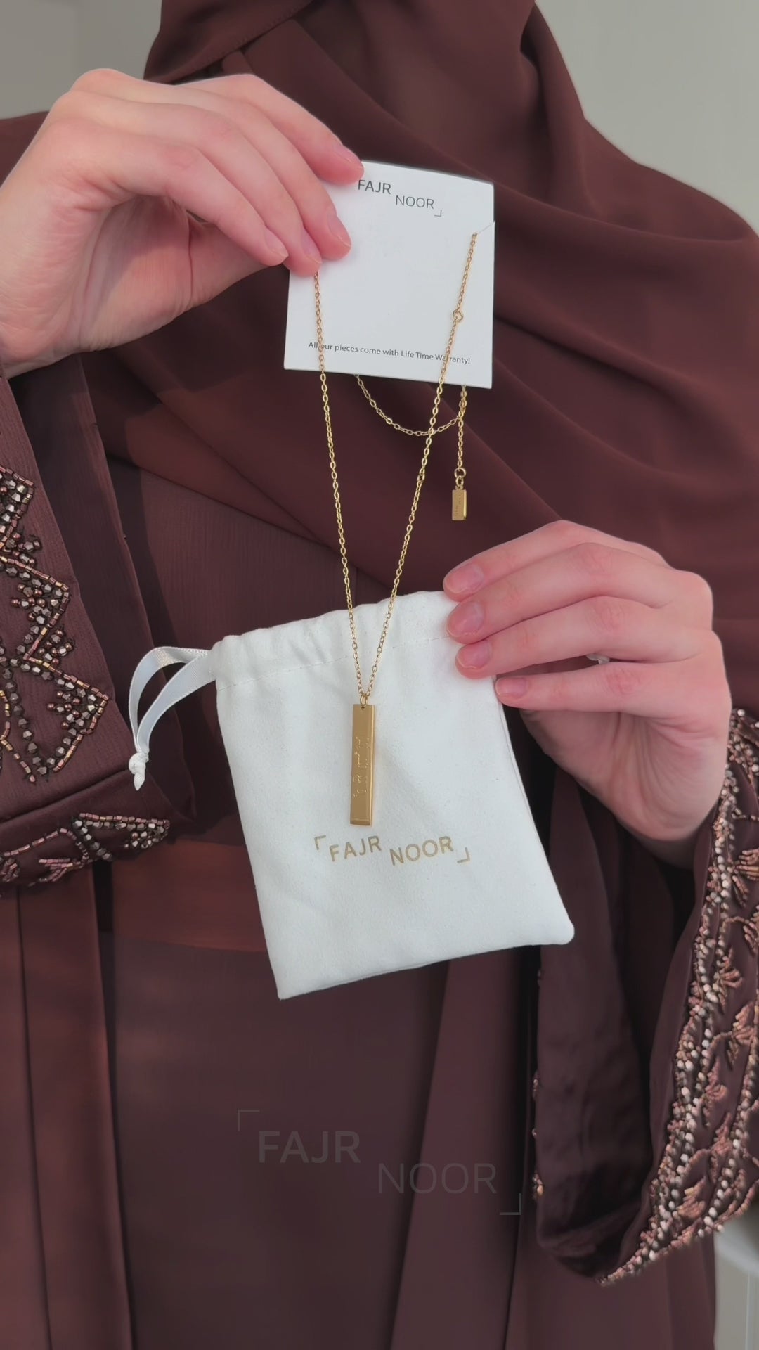 Woman wearing the Fajr Noor Maryam Eid Abaya in royal coffee, unboxing gold bar necklaces