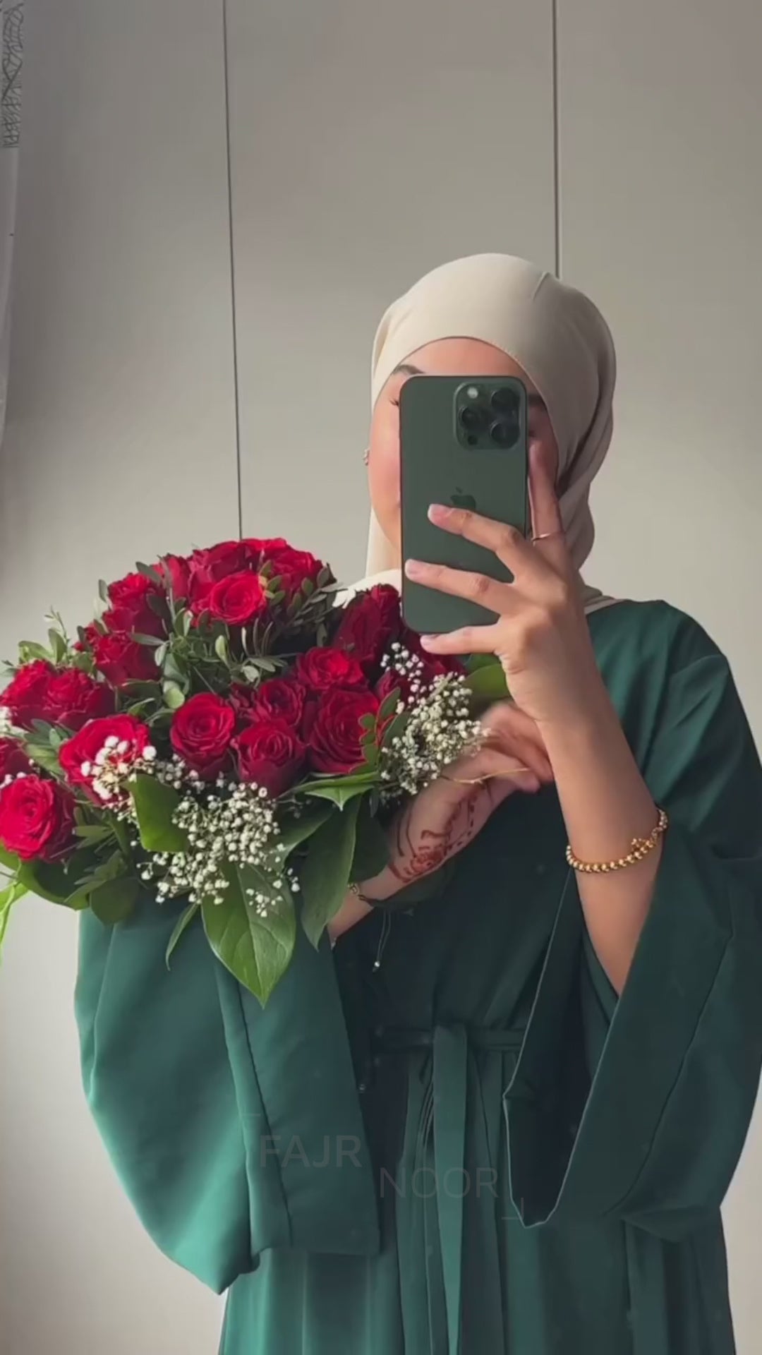 Woman wearing the Fajr Noor Khatijah Abaya in emerald with a taupe hijab, holding a bouquet of red roses