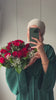 Woman wearing the Fajr Noor Khatijah Abaya in emerald with a taupe hijab, holding a bouquet of red roses